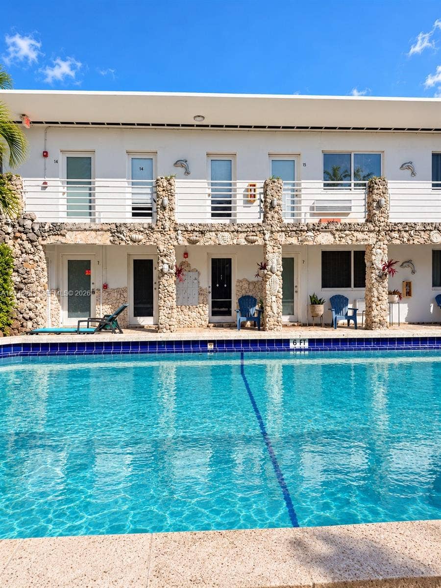 320 85th Street, #22, Miami Beach, FL 33141 Swimming pool with blue tile edging and stone-textured coping, featuring a two-story exterior facade with stone pillars and horizontal metal railing