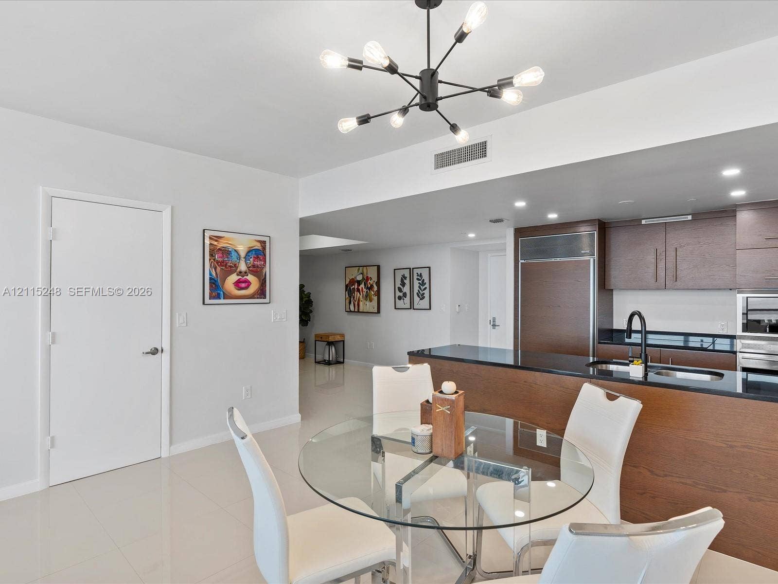 Modern kitchen featuring dark wood-finish cabinetry, a black stone countertop, integrated refrigerator, and an eight-light matte black chandelier