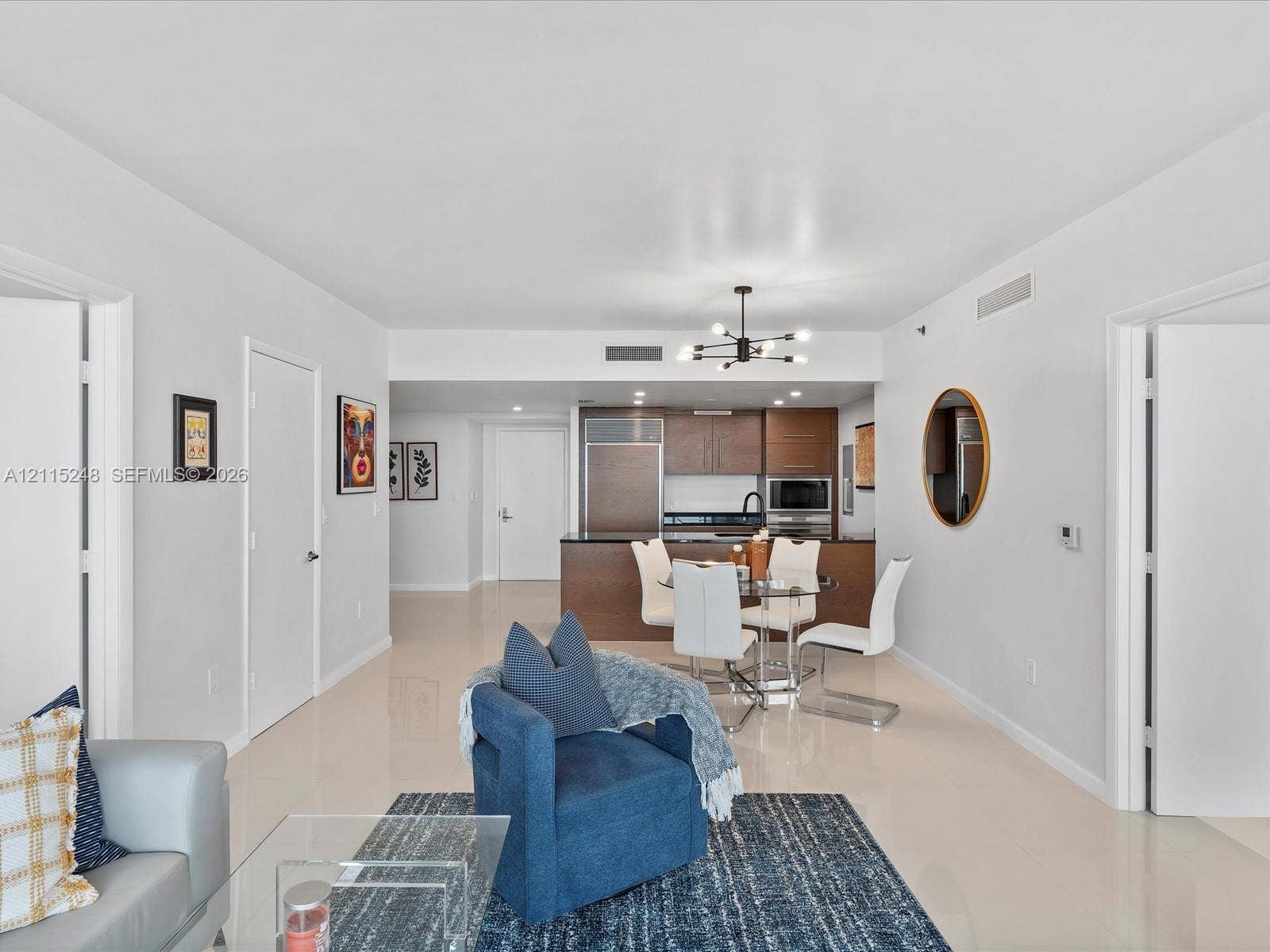 Open floor plan featuring light-toned tile flooring, recessed ceiling lighting, contemporary multi-arm chandelier, and kitchen cabinetry with integrated appliances