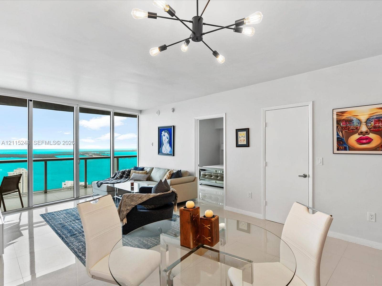 Floor-to-ceiling sliding glass doors, water backdrop, large-format tile flooring, multi-arm sputnik-style chandelier, and recessed lighting