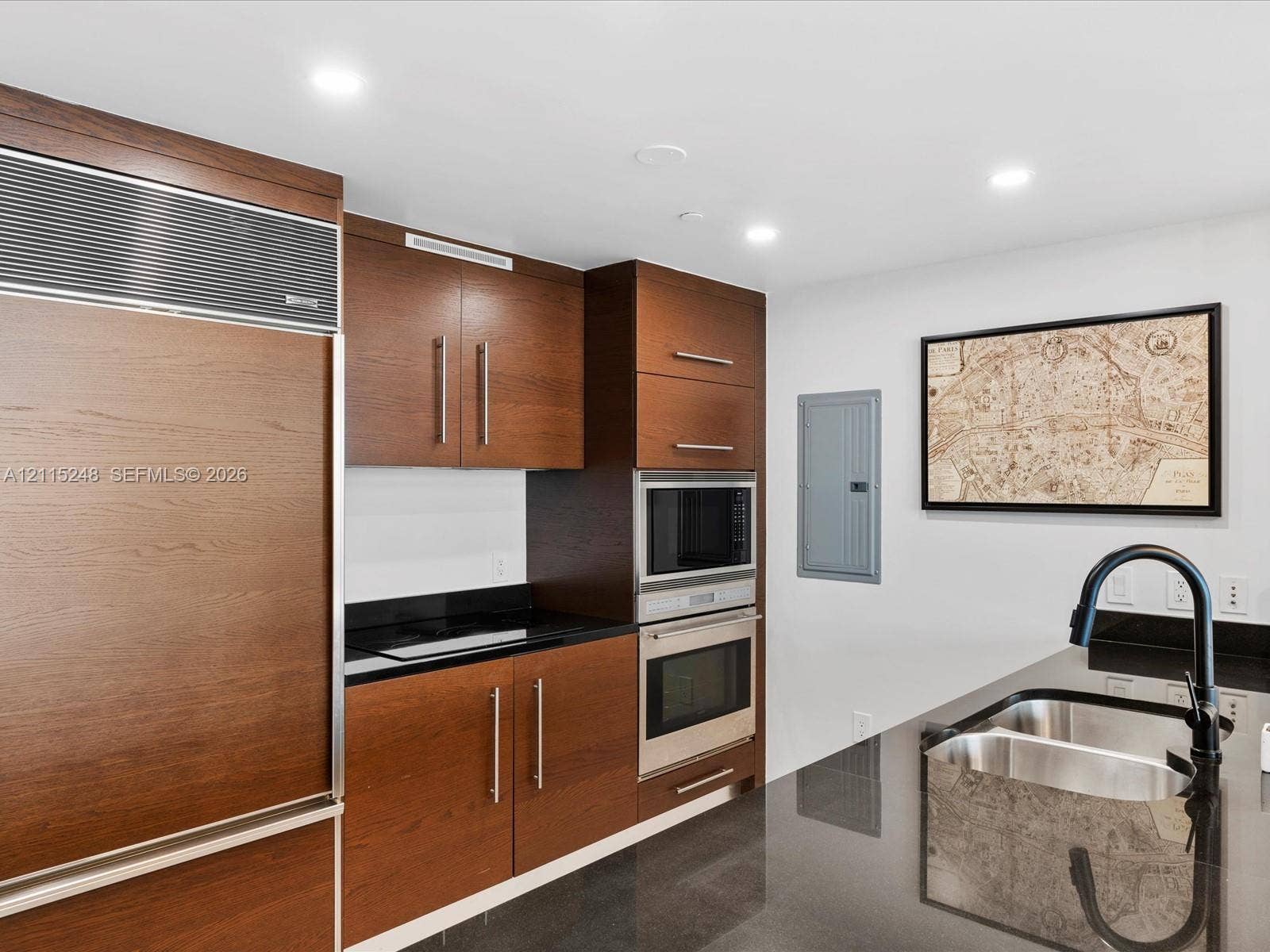 Kitchen featuring dark wood-finish cabinetry, built-in stainless steel double wall ovens, panel-ready refrigerator, polished stone countertops, and a matte black gooseneck faucet