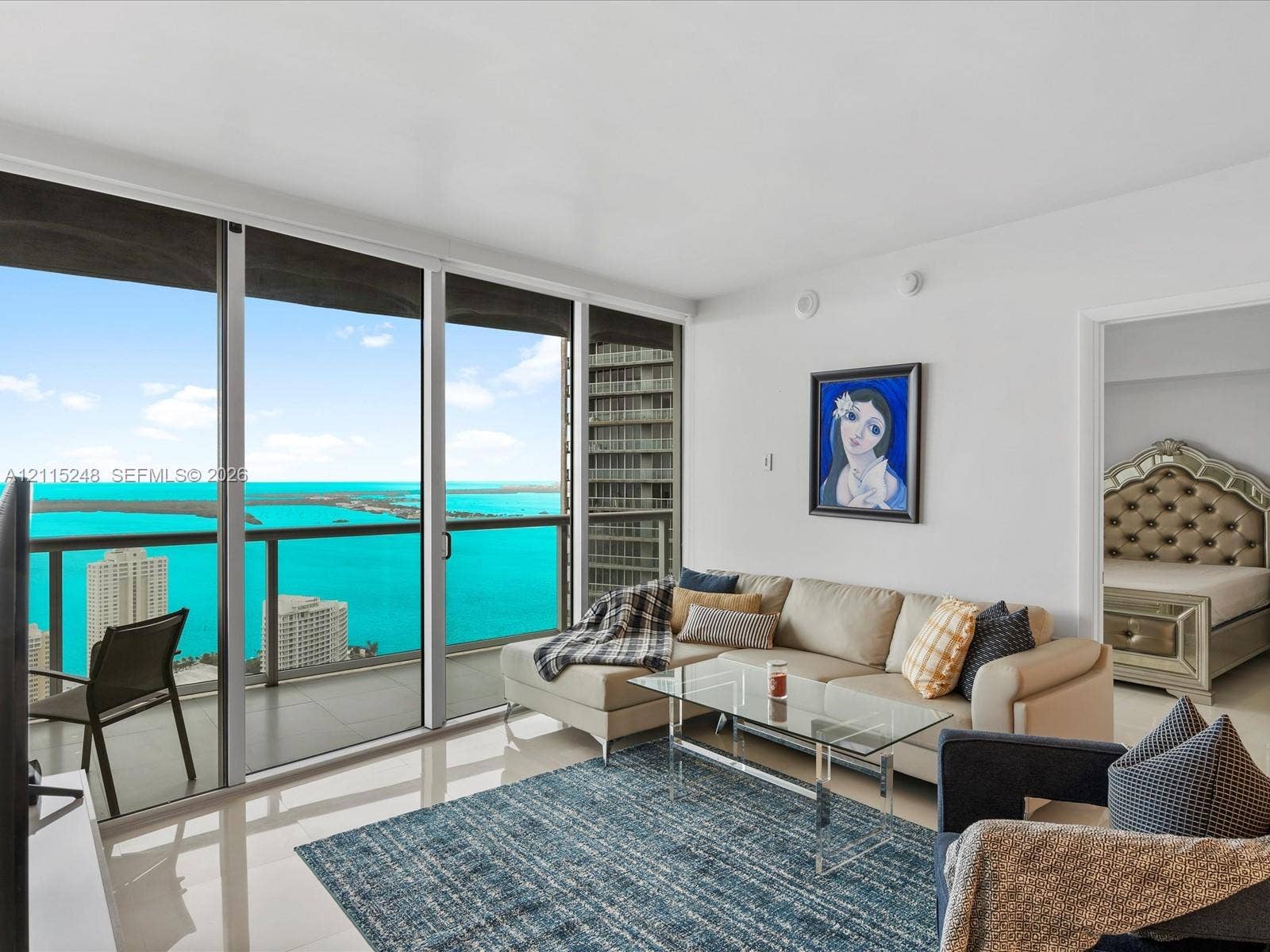 Floor-to-ceiling sliding glass panels, balcony with metal railing, polished neutral-toned flooring, and expansive water scenery
