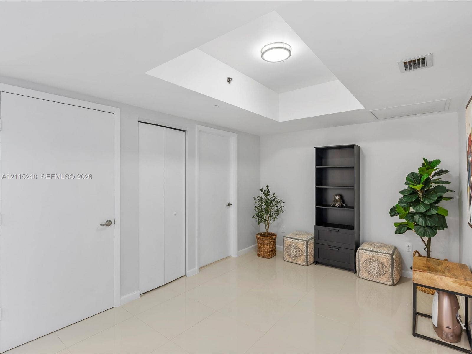 Interior space featuring a recessed tray ceiling, neutral tile flooring, and multiple closet enclosures with flush-panel doors