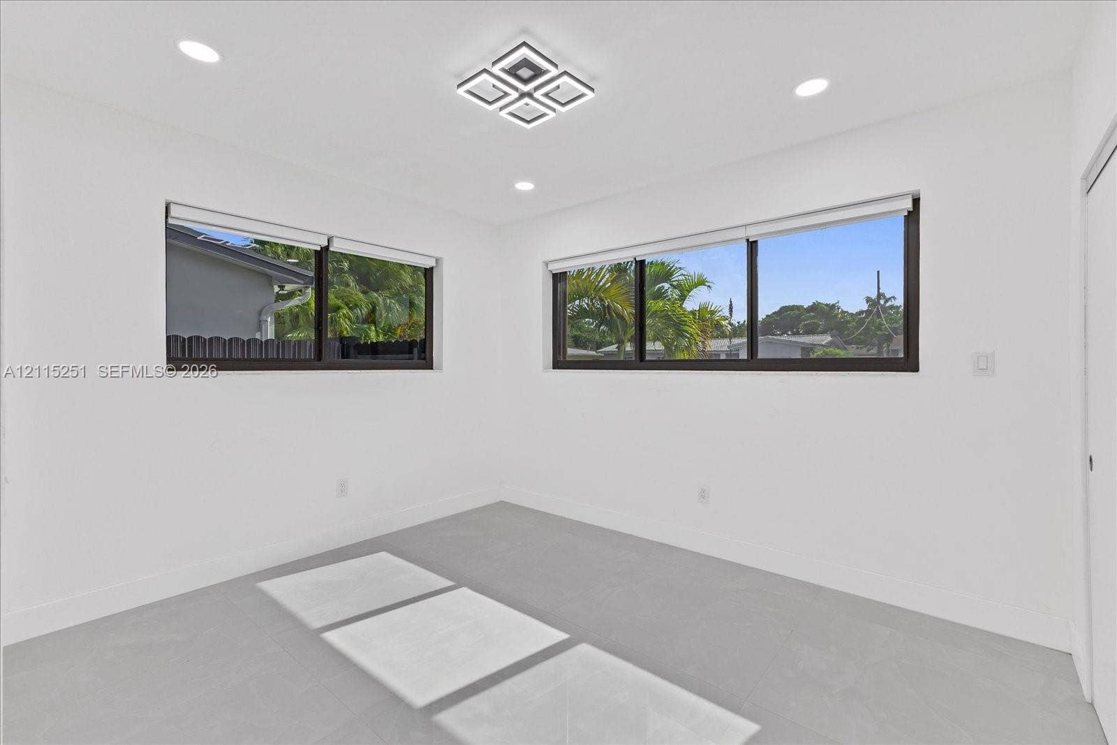 19511 NE 18th Place, Miami, FL 33179 Interior room featuring neutral wall finishes, large dual-pane windows with dark frames, matte light gray tile flooring, recessed ceiling lighting, and a modern geometric flush-mount light fixture