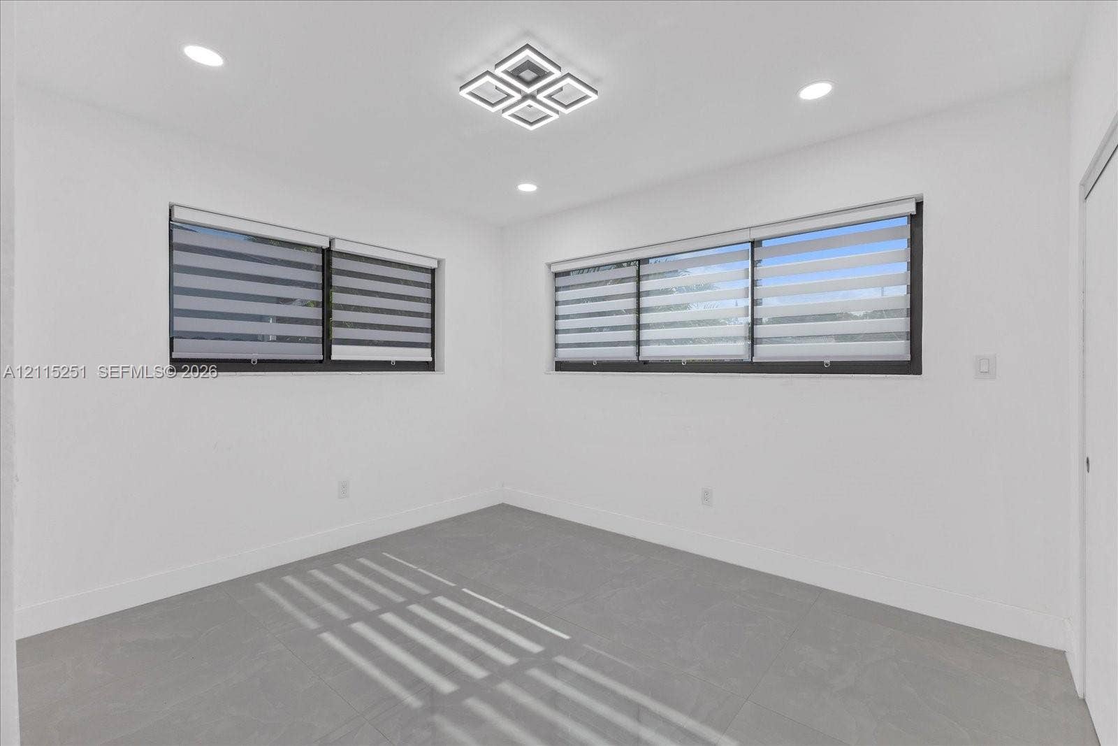 19511 NE 18th Place, Miami, FL 33179 Neutral-toned room featuring large-format tile flooring, recessed ceiling lighting, a modern geometric flush-mount light fixture, and windows equipped with dual-layered roller shades
