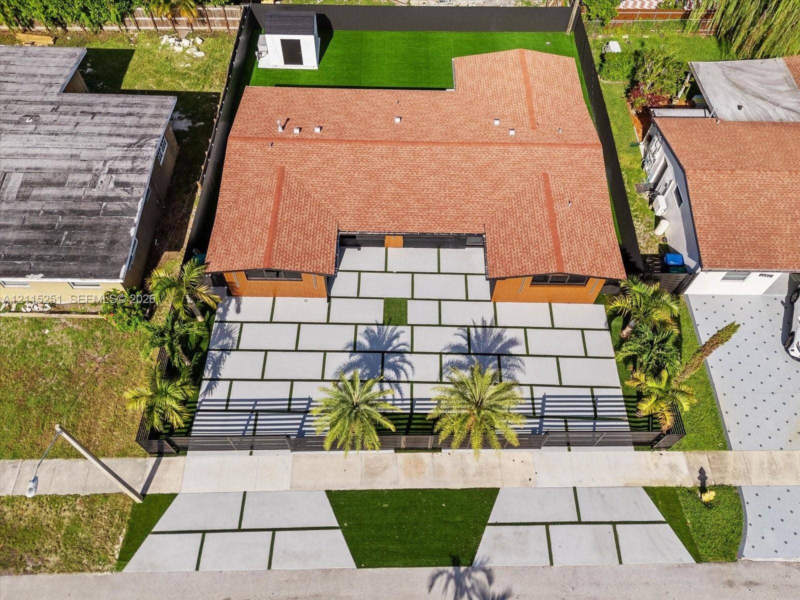 19511 NE 18th Place, Miami, FL 33179 Aerial view of residential property featuring a large-format paver driveway, synthetic turf lawn, perimeter fencing, and mature palm trees