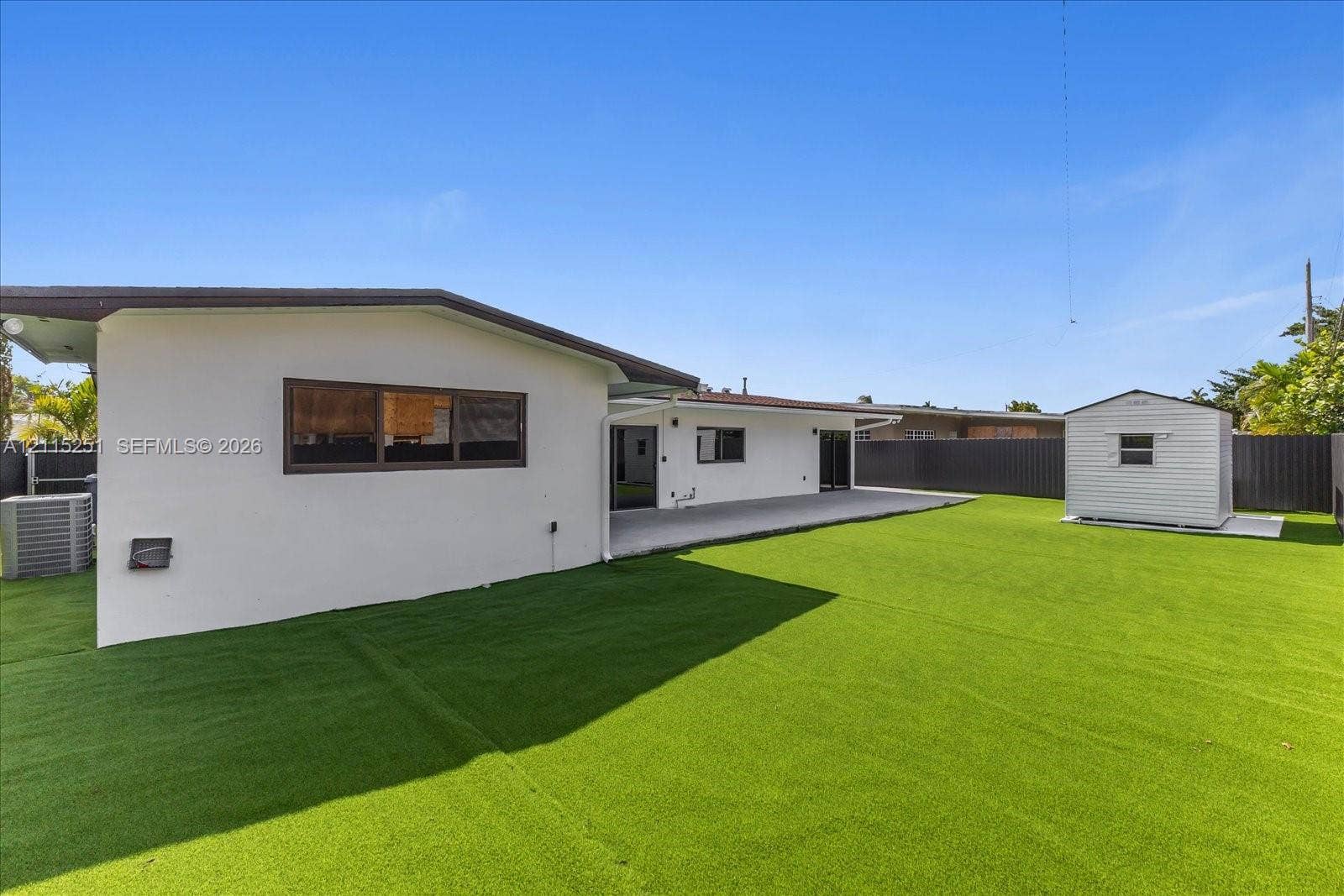 19511 NE 18th Place, Miami, FL 33179 Backyard featuring low-maintenance synthetic turf, a concrete patio, perimeter privacy fencing, and a detached storage shed
