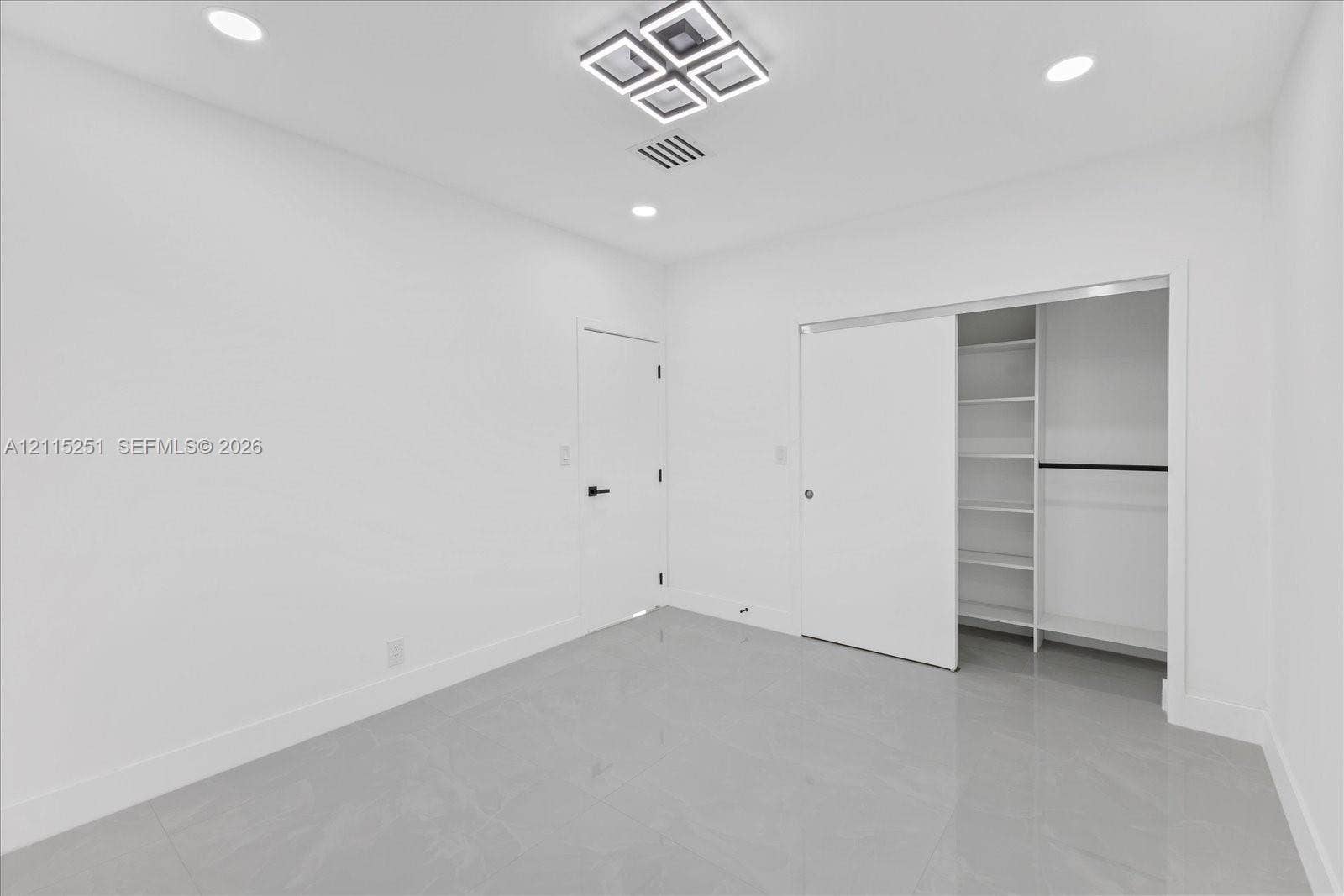 19511 NE 18th Place, Miami, FL 33179 Bright room featuring polished tile flooring, recessed lighting, a modern geometric ceiling fixture, and a sliding closet door with integrated shelving