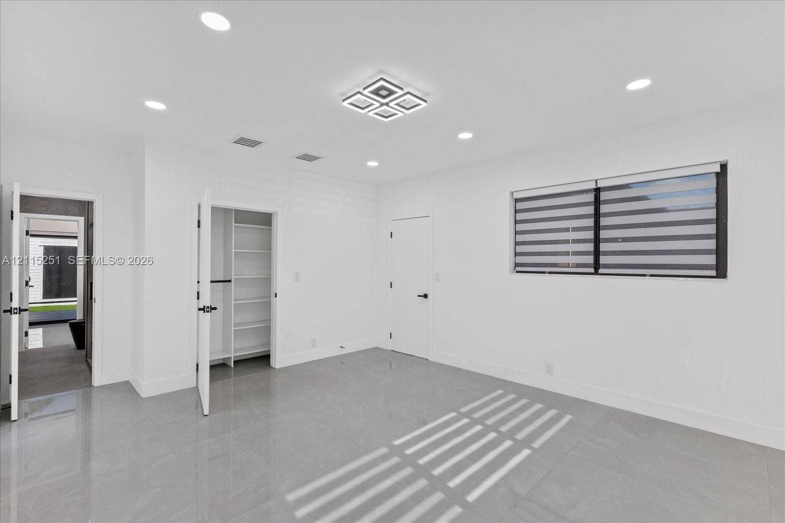 19511 NE 18th Place, Miami, FL 33179 Interior space featuring large-format tile flooring, recessed ceiling lighting, a tiered geometric light fixture, and a built-in closet with integrated shelving