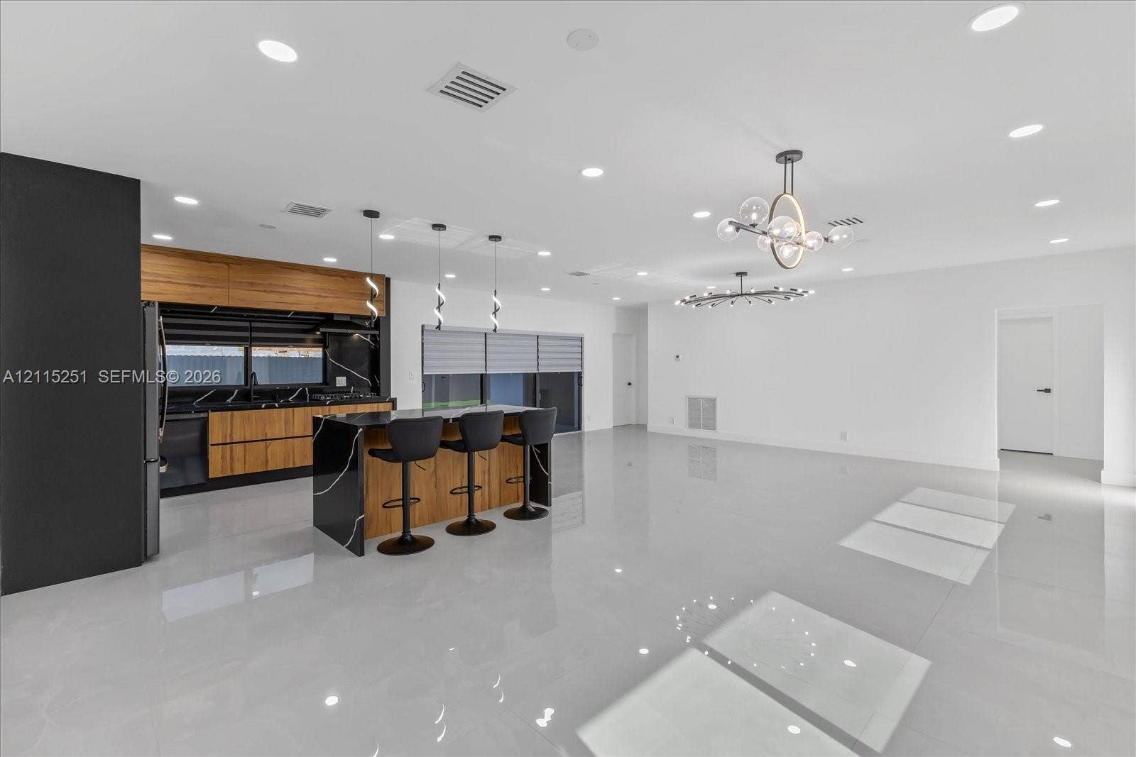 19511 NE 18th Place, Miami, FL 33179 Kitchen featuring a large central island with waterfall-edge stone countertops, wood-finish cabinetry, black stone backsplash, recessed lighting, and modern multi-light chandeliers