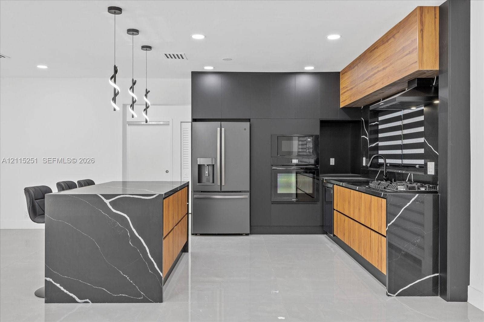 19511 NE 18th Place, Miami, FL 33179 Kitchen featuring a waterfall island with dark veined stone surfacing, flat-panel wood-finish cabinetry, built-in stainless steel appliances, matte black fixtures, and modern pendant lighting
