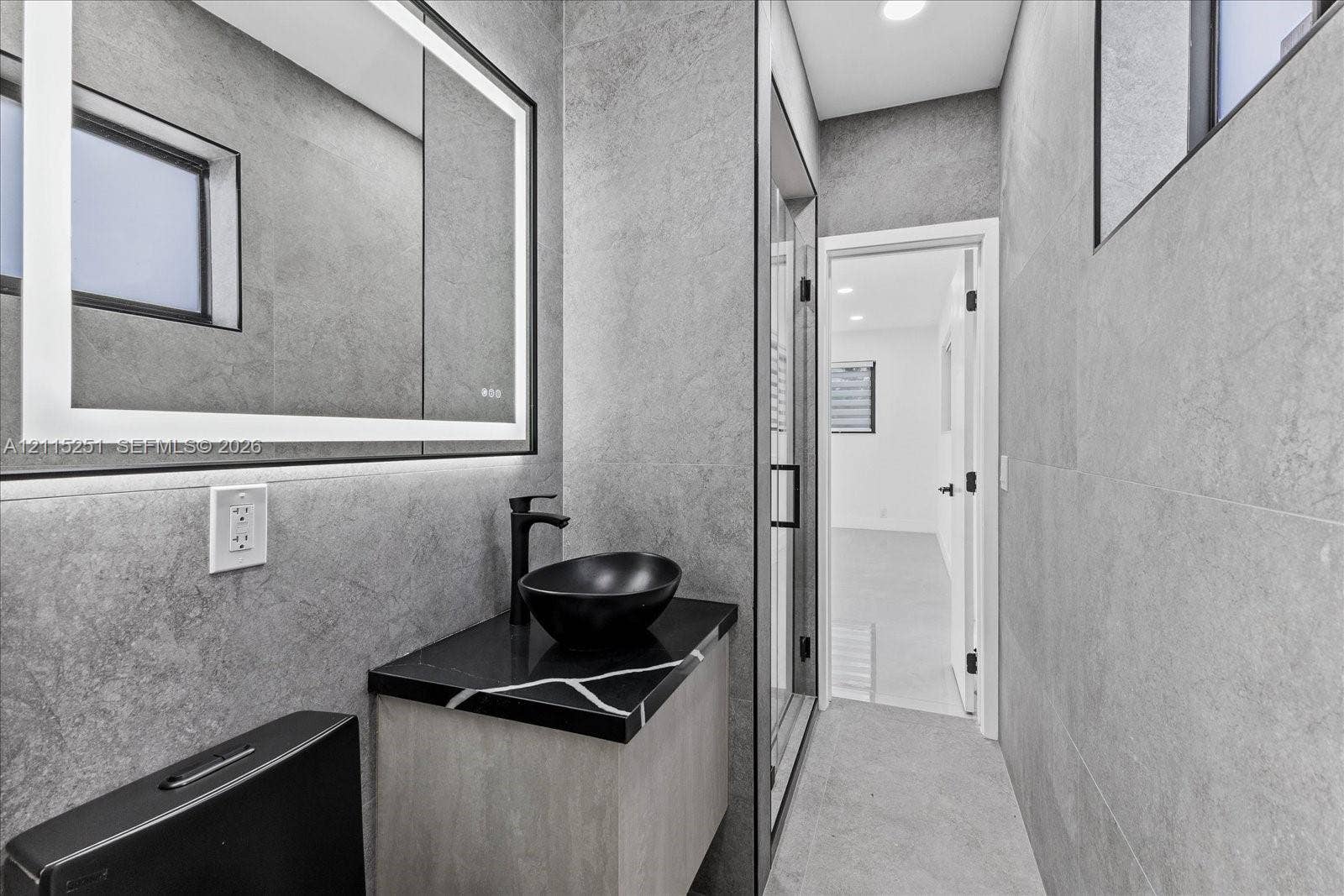 19511 NE 18th Place, Miami, FL 33179 Modern vanity featuring a stone-finish countertop, black vessel sink, matte black faucet, integrated LED-backlit mirror, and floor-to-ceiling stone-style wall tile