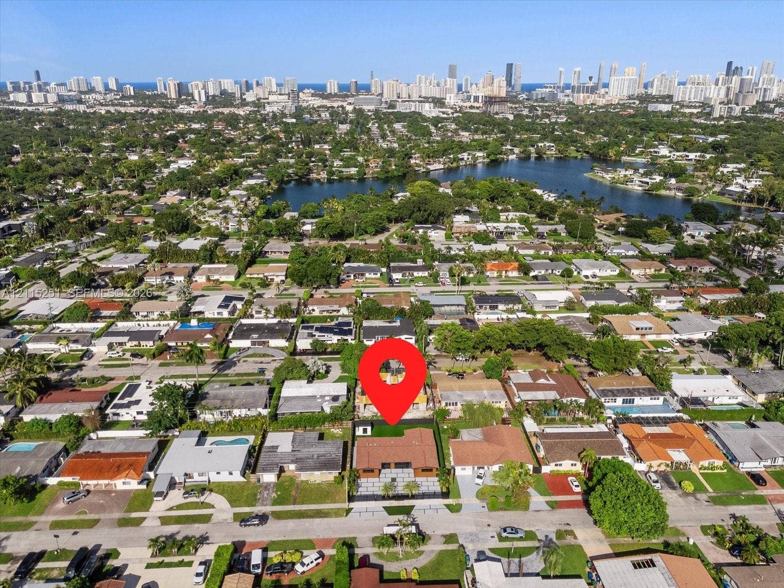 19511 NE 18th Place, Miami, FL 33179 Aerial perspective showcasing a residential property with a paved driveway, rectangular roofline, and rear outdoor space including a swimming pool, all set within a coastal urban environment