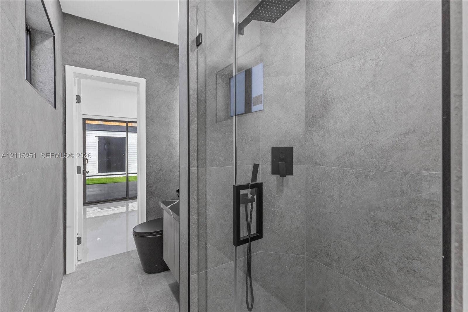 19511 NE 18th Place, Miami, FL 33179 Walk-in glass-enclosed shower featuring large-format gray tile, a rainfall showerhead, and matte black fixtures, complemented by a floor-mounted toilet and a gray vanity cabinet