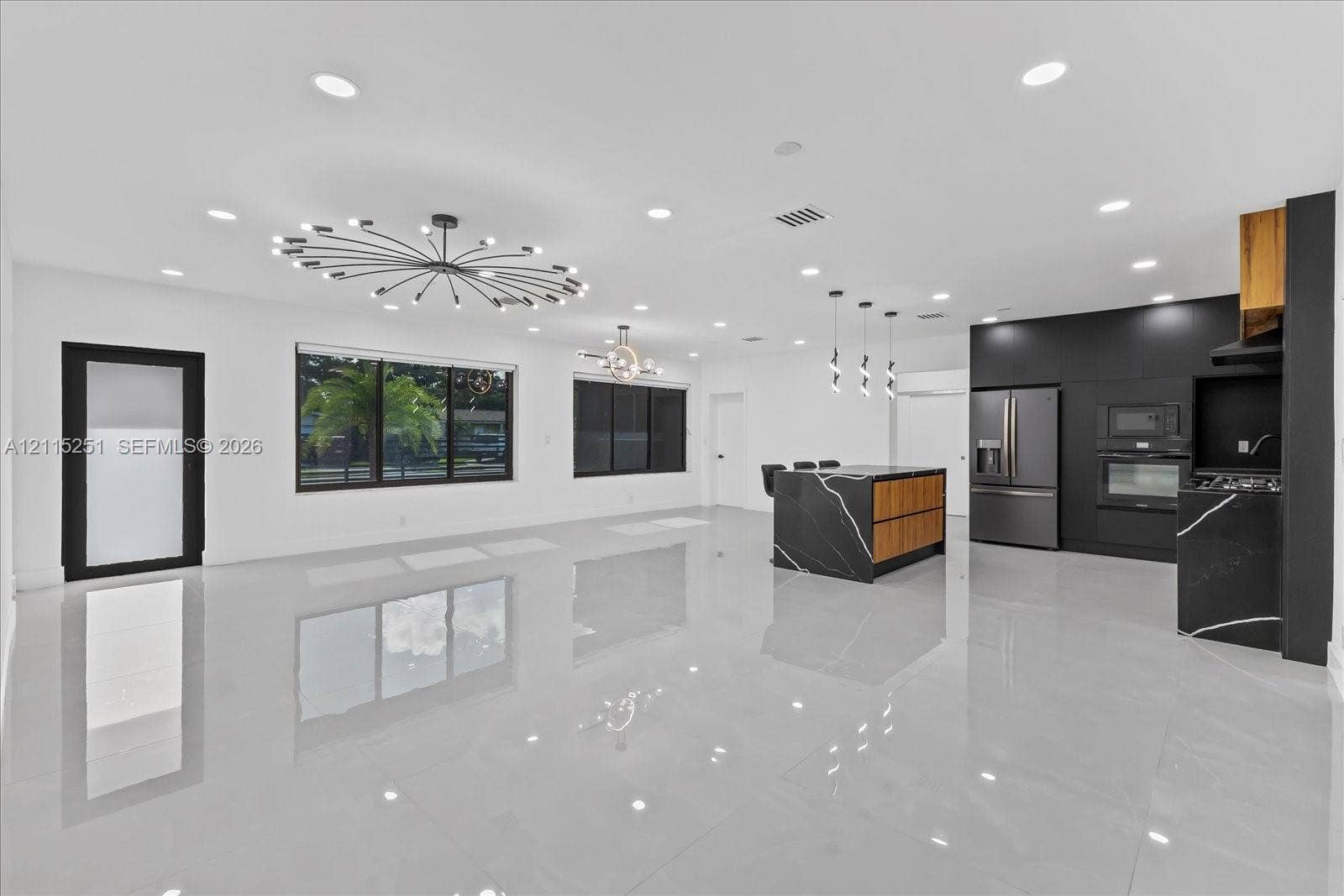 19511 NE 18th Place, Miami, FL 33179 Open-concept living space featuring high-gloss tile flooring, recessed lighting, matte black cabinetry, and a kitchen island with stone-finish surfaces and wood-tone accents