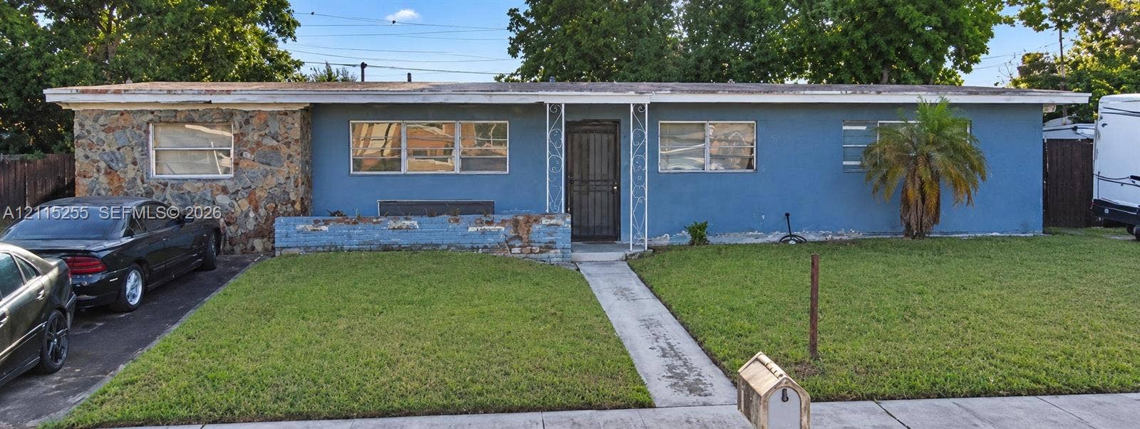 Miami Gardens, FL 33055 Single-story exterior featuring a stone-clad facade, blue painted siding, horizontal windows, a decorative metal porch support, and a concrete walkway