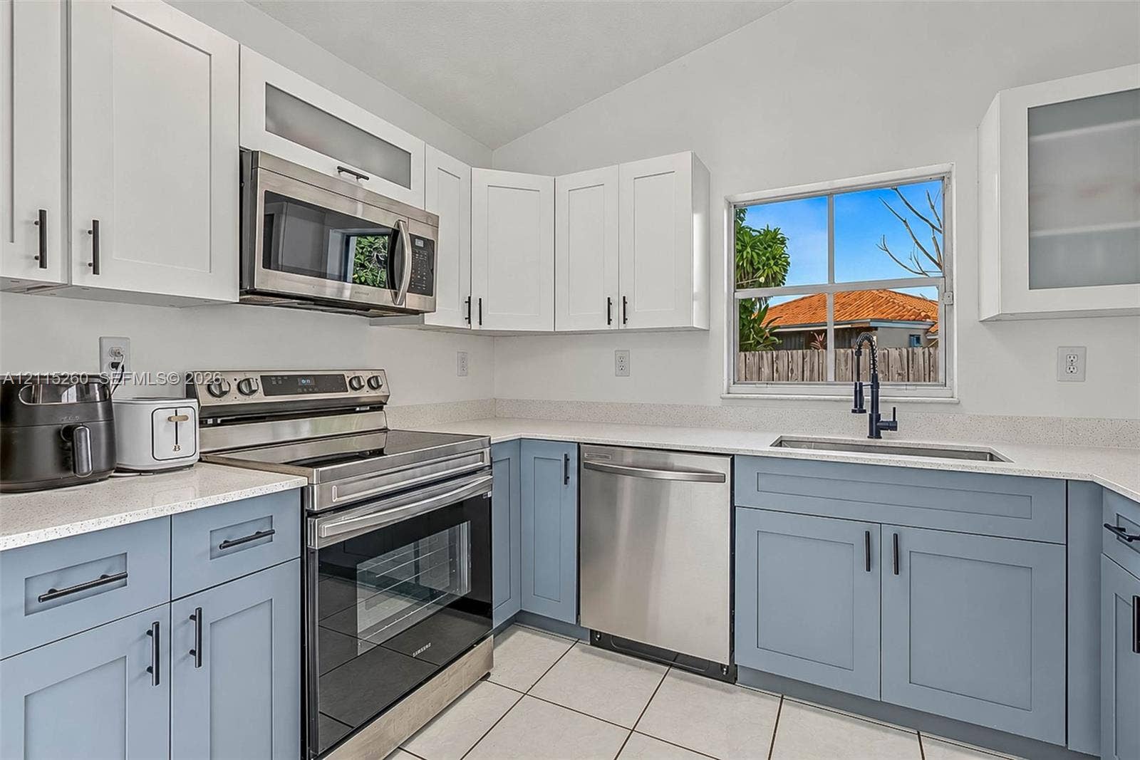 820 NW 132nd Court, Miami, FL 33182 Two-toned cabinetry with upper white shaker-style cabinets and lower blue shaker-style cabinets, light-toned stone-finish countertops, stainless steel appliances, and a single-basin undermount sink with a matte black faucet