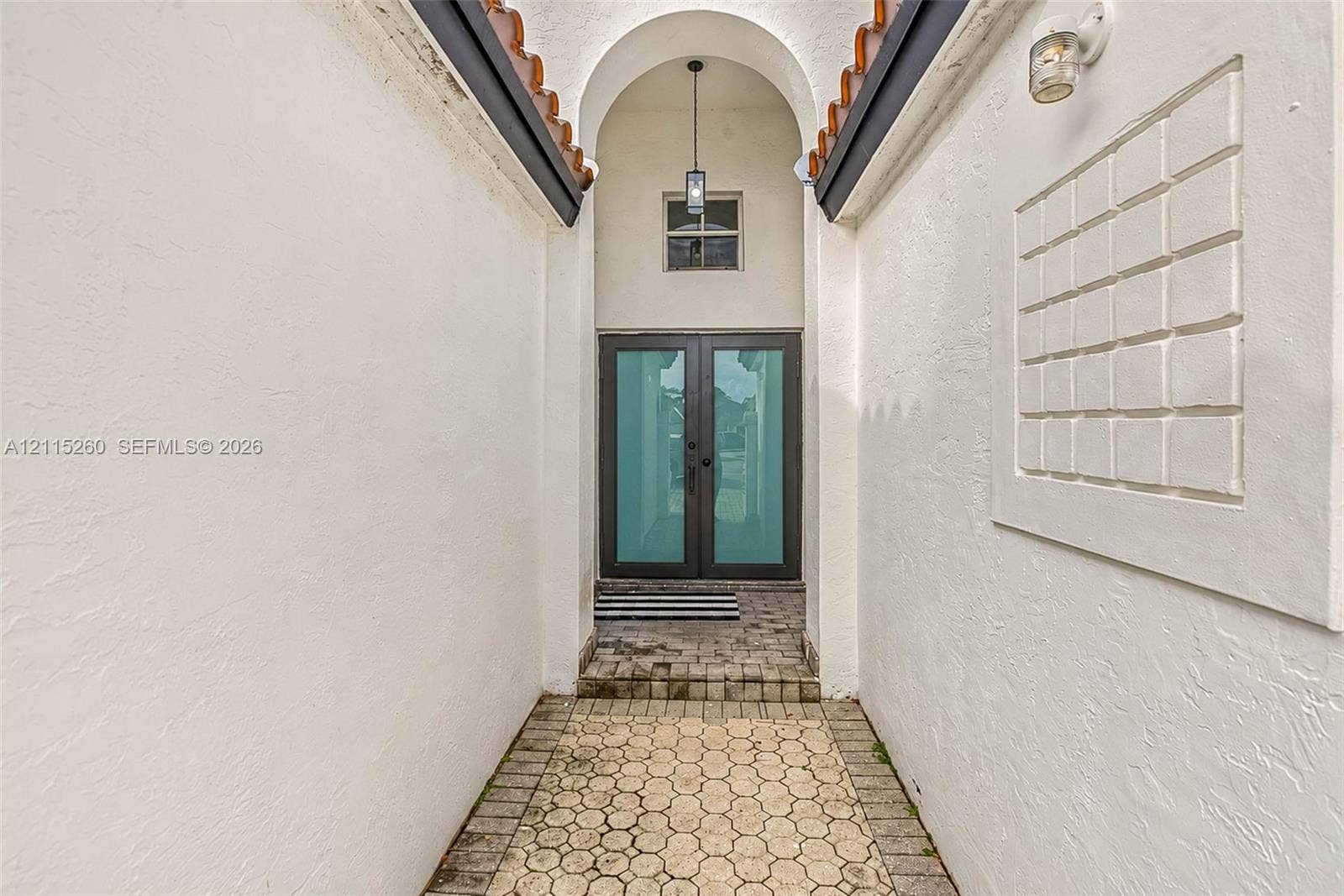 820 NW 132nd Court, Miami, FL 33182 Entryway featuring a double-door entrance with glass panels, an arched ceiling with a pendant light, a recessed square wall relief, and paver stone flooring