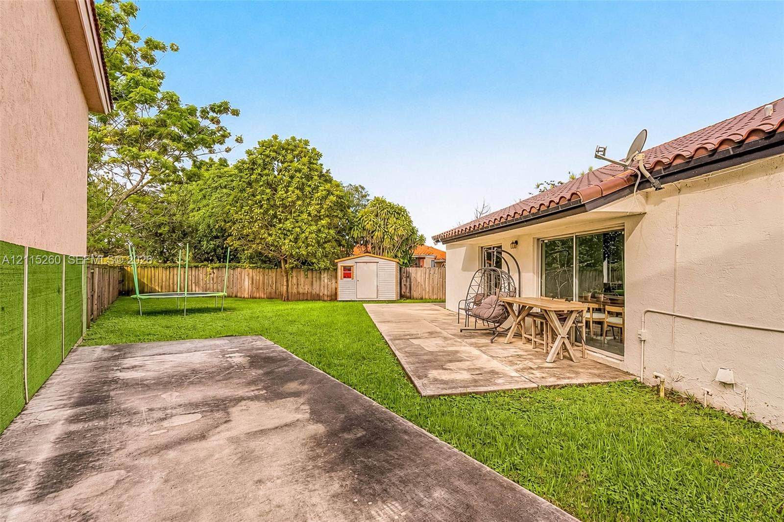 820 NW 132nd Court, Miami, FL 33182 Backyard featuring a concrete patio, grassy lawn, wood privacy fencing, and a detached storage shed