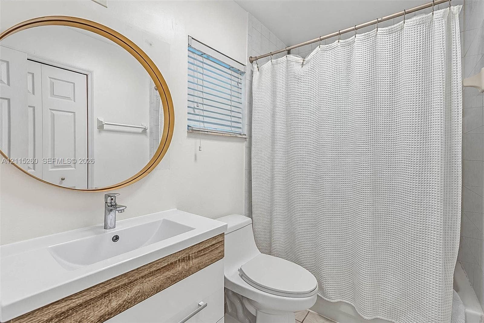 820 NW 132nd Court, Miami, FL 33182 Bathroom featuring a white vanity with wood-finish detailing, integrated rectangular sink, round mirror with a metallic frame, and a tub-shower combination with tile surround