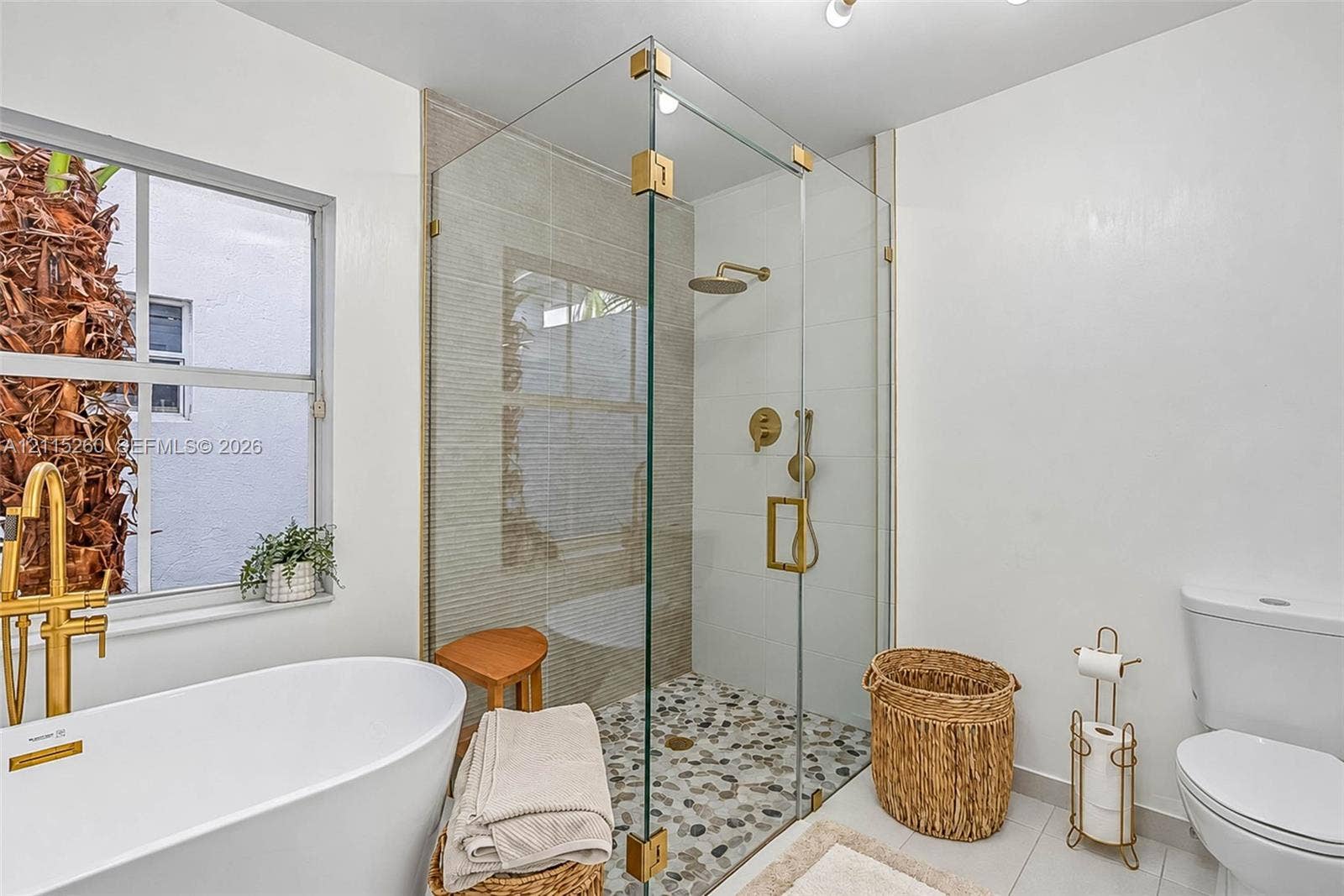 820 NW 132nd Court, Miami, FL 33182 Freestanding soaking tub with a brass-finish floor-mounted faucet, frameless glass-enclosed shower with a pebble stone floor, and brass-finish shower fixtures