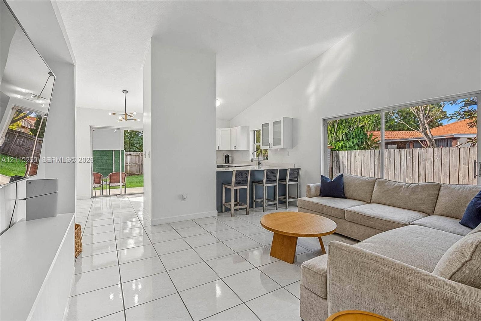 820 NW 132nd Court, Miami, FL 33182 Open-concept living space featuring vaulted ceilings, large-format tile flooring, sliding glass patio doors, and a kitchen equipped with a breakfast bar and white upper cabinetry