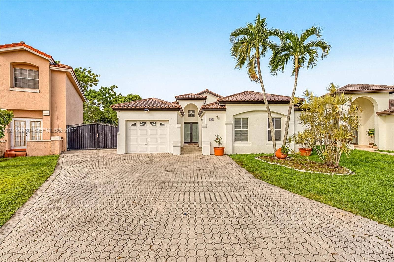 820 NW 132nd Court, Miami, FL 33182 Stucco exterior with a tiled roof, paver driveway, attached garage, and landscaping featuring mature palms