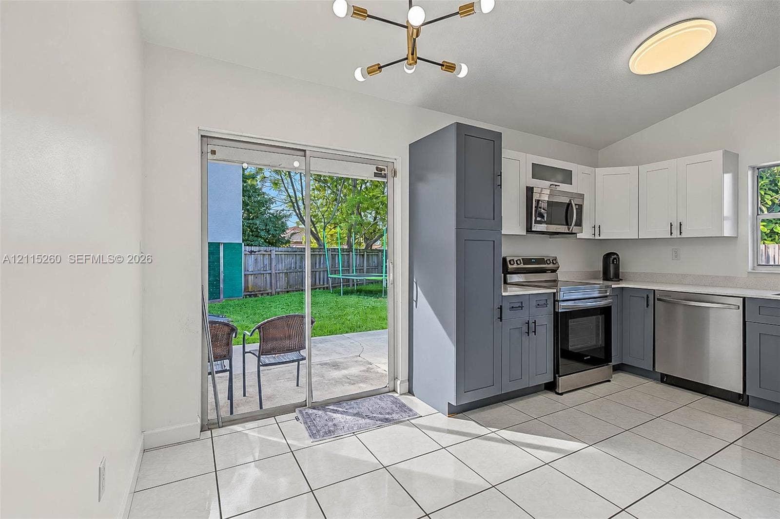 820 NW 132nd Court, Miami, FL 33182 Kitchen featuring two-tone cabinetry, stainless steel appliances, white tile flooring, a multi-arm geometric light fixture, and a sliding glass door