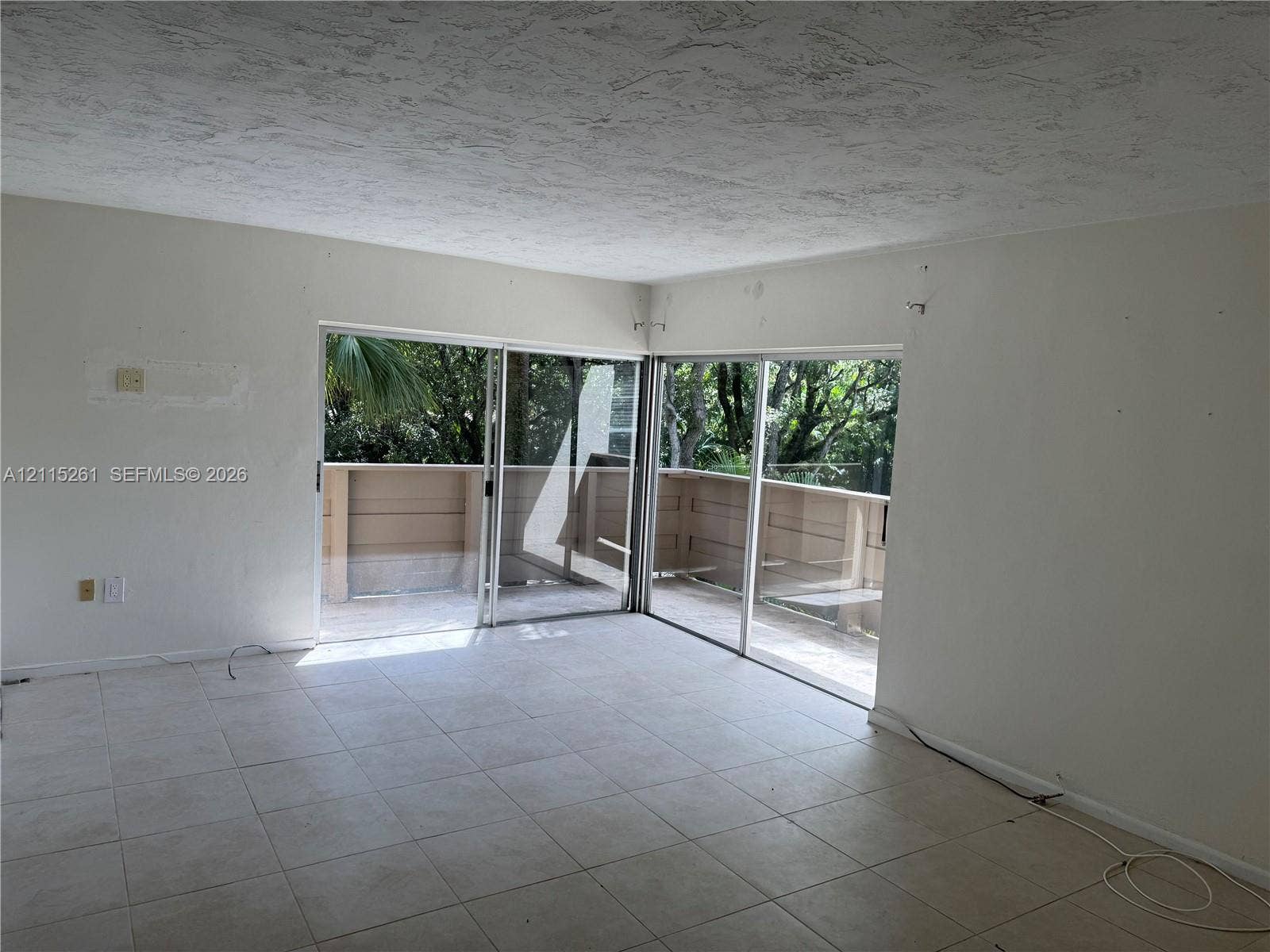 1205 Mariposa Avenue, #302, Coral Gables, Coral Gables, FL 33146 Interior space featuring ceramic tile flooring, neutral wall finishes, and dual glass sliding doors opening to a wrap-around balcony with solid privacy railing