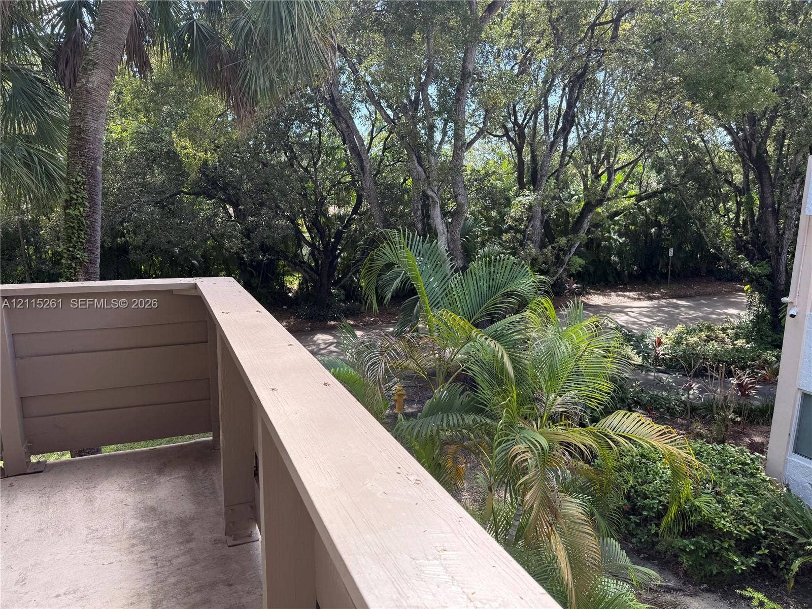 1205 Mariposa Avenue, #302, Coral Gables, Coral Gables, FL 33146 Covered balcony featuring wood-tone railings and concrete flooring, overlooking mature trees and lush landscaping