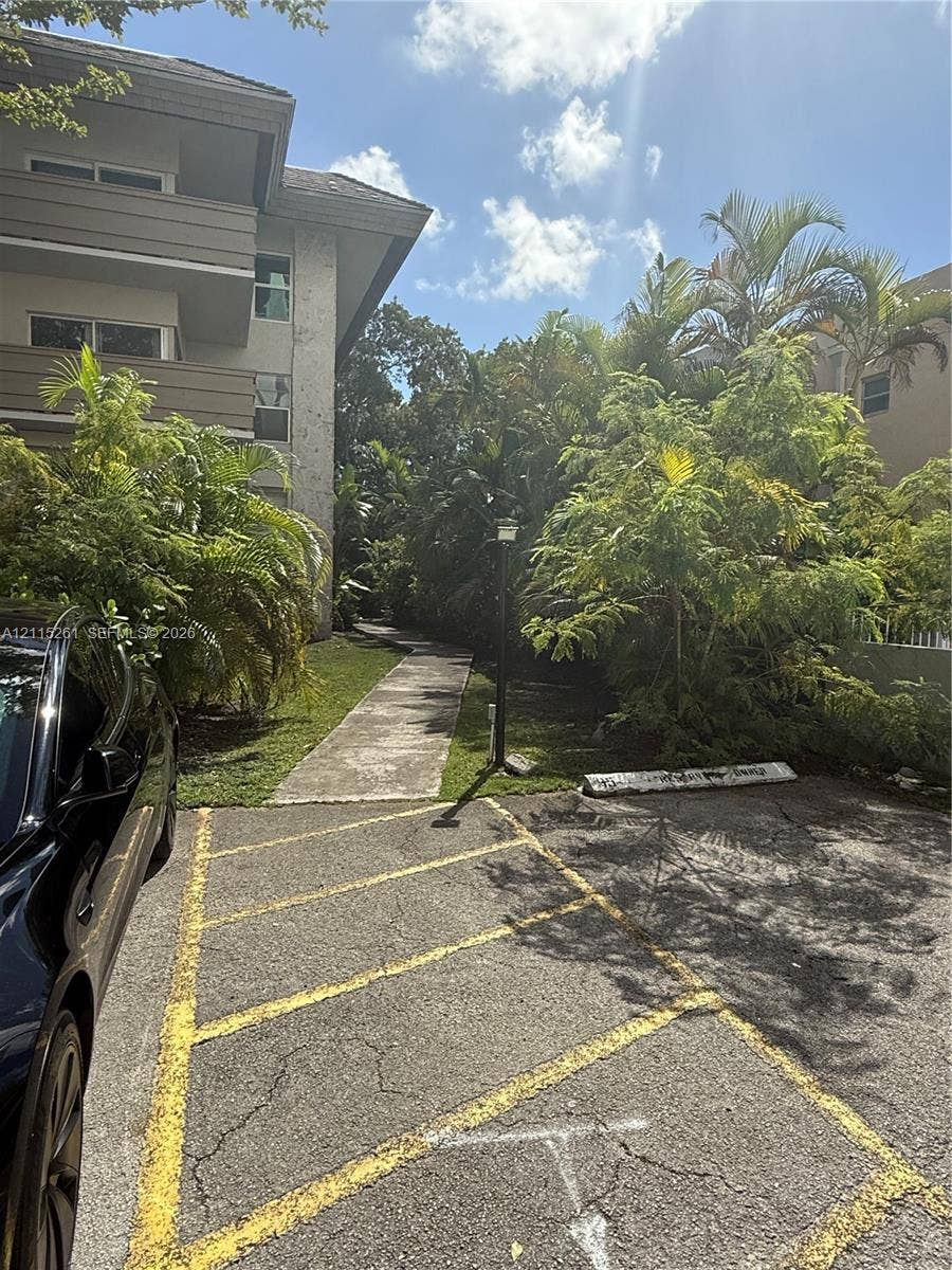 1205 Mariposa Avenue, #302, Coral Gables, Coral Gables, FL 33146 Multi-story building exterior featuring concrete walkways, paved parking area with marked stalls, and mature landscaping