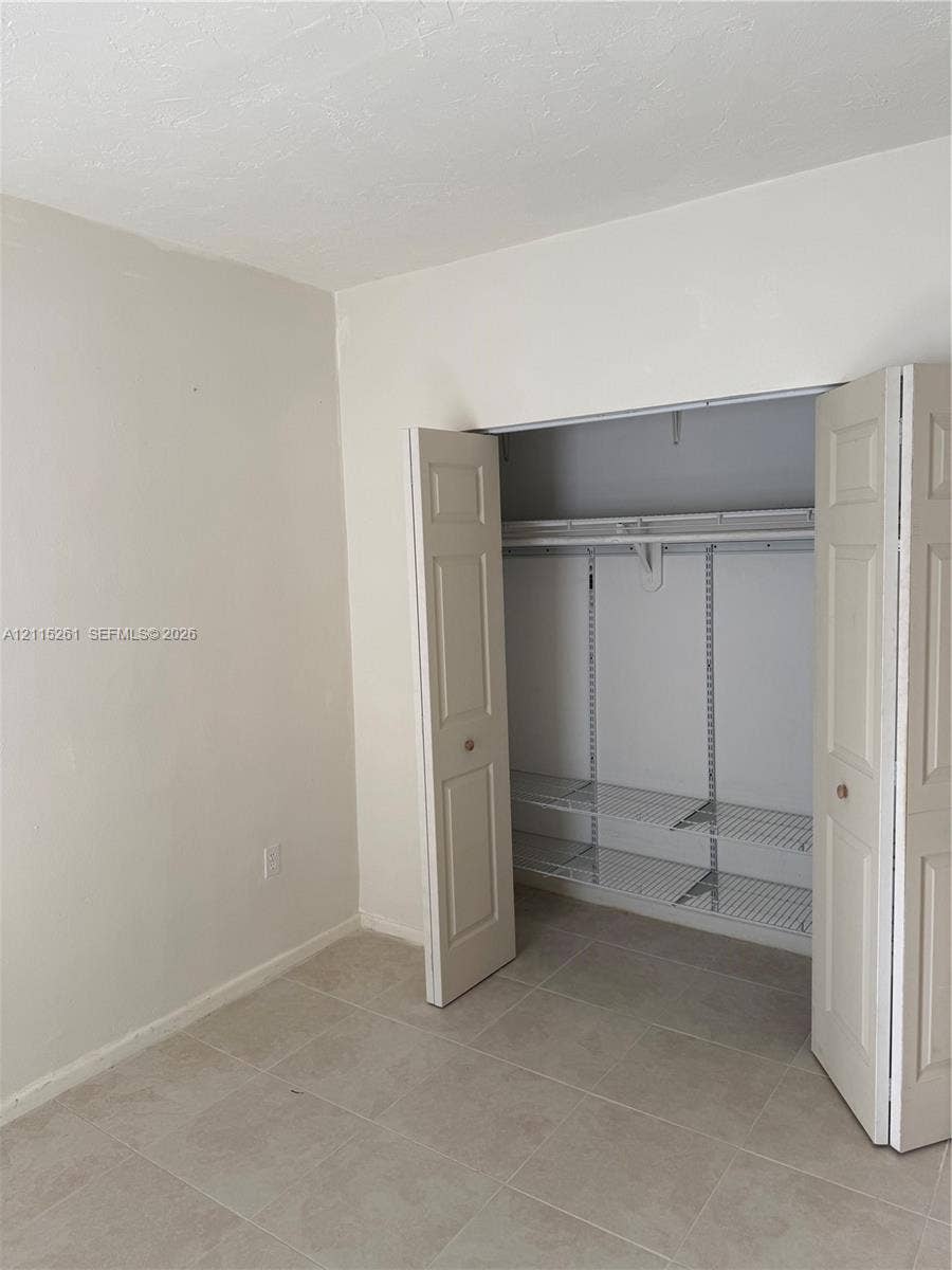 1205 Mariposa Avenue, #302, Coral Gables, Coral Gables, FL 33146 Neutral-toned interior space featuring light-colored tile flooring and a built-in closet with paneled bifold doors, an integrated hanging rod, and adjustable wire shelving