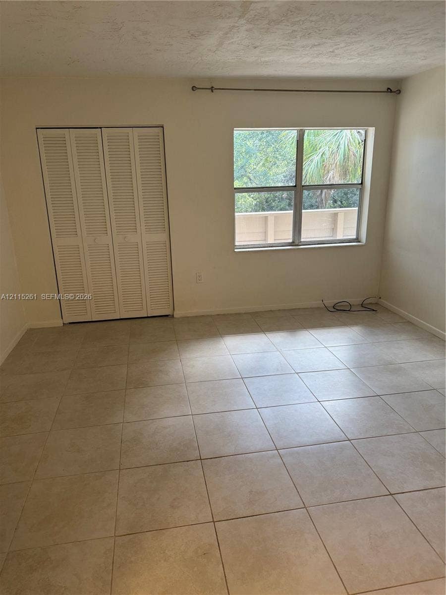 1205 Mariposa Avenue, #302, Coral Gables, Coral Gables, FL 33146 Neutral-toned tile flooring, white bi-fold closet doors, and a single-pane window with a curtain rod