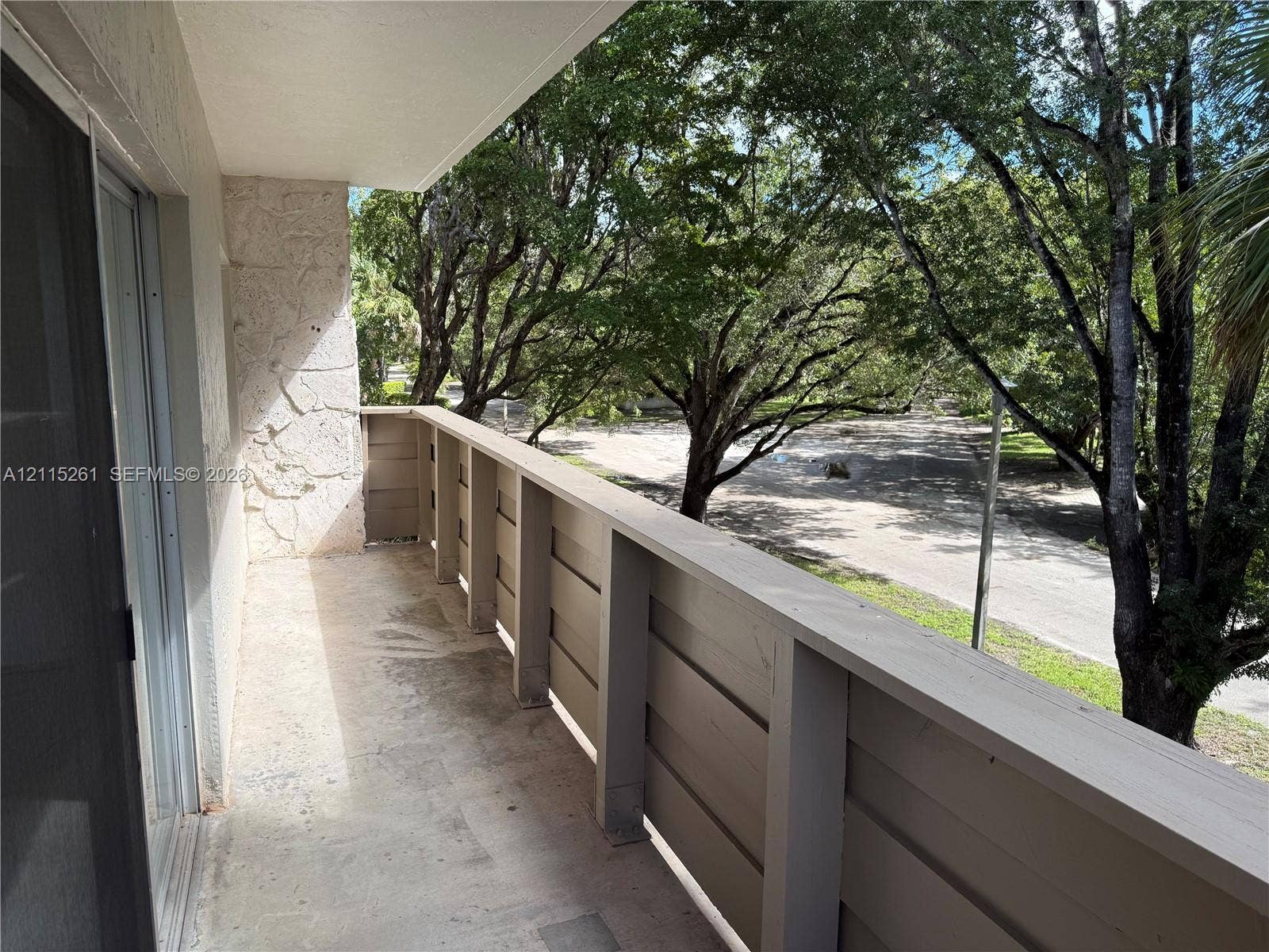 1205 Mariposa Avenue, #302, Coral Gables, Coral Gables, FL 33146 Private balcony featuring a concrete floor, horizontal wood-style railing, and natural stone wall accents, framed by mature trees