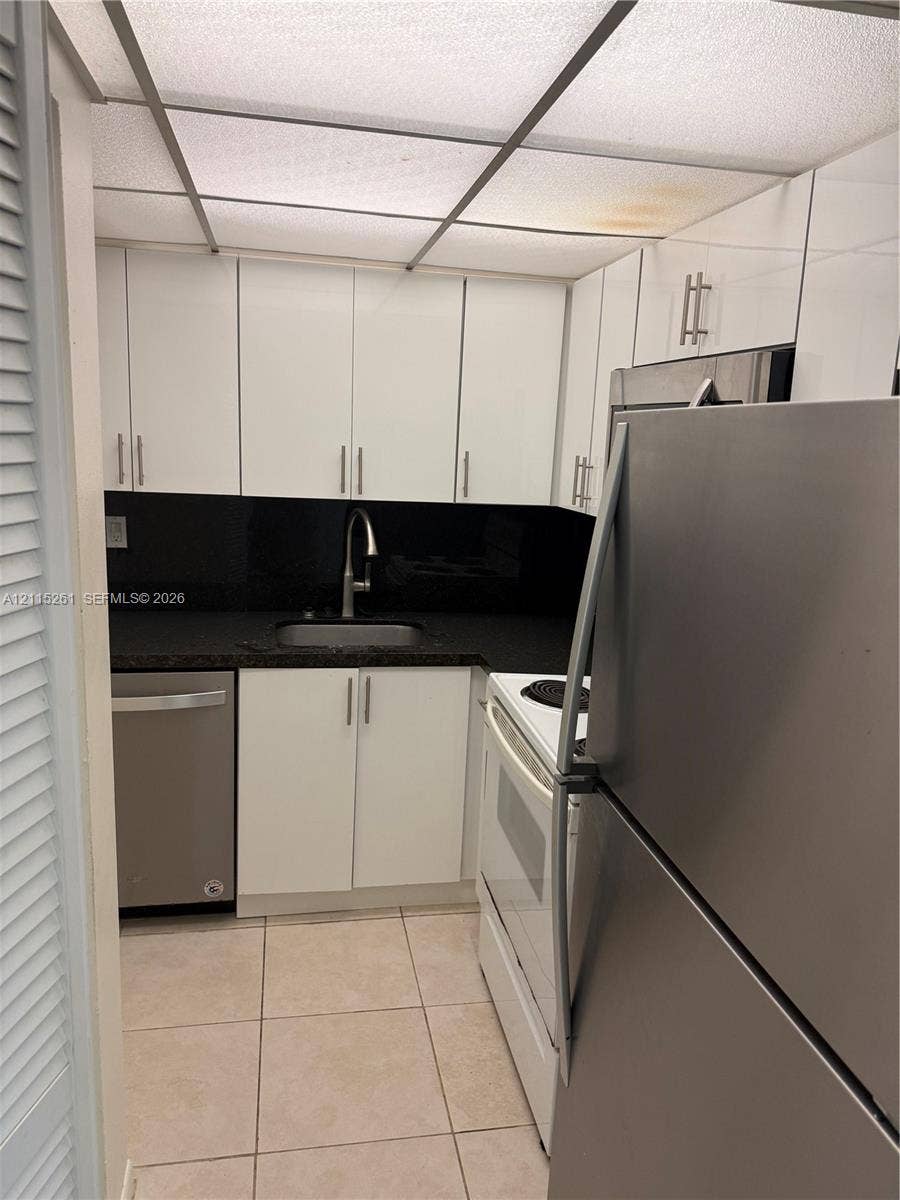 1205 Mariposa Avenue, #302, Coral Gables, Coral Gables, FL 33146 Kitchen featuring white flat-panel cabinetry, dark stone countertops, stainless steel appliances, a chrome gooseneck faucet, and tiled flooring