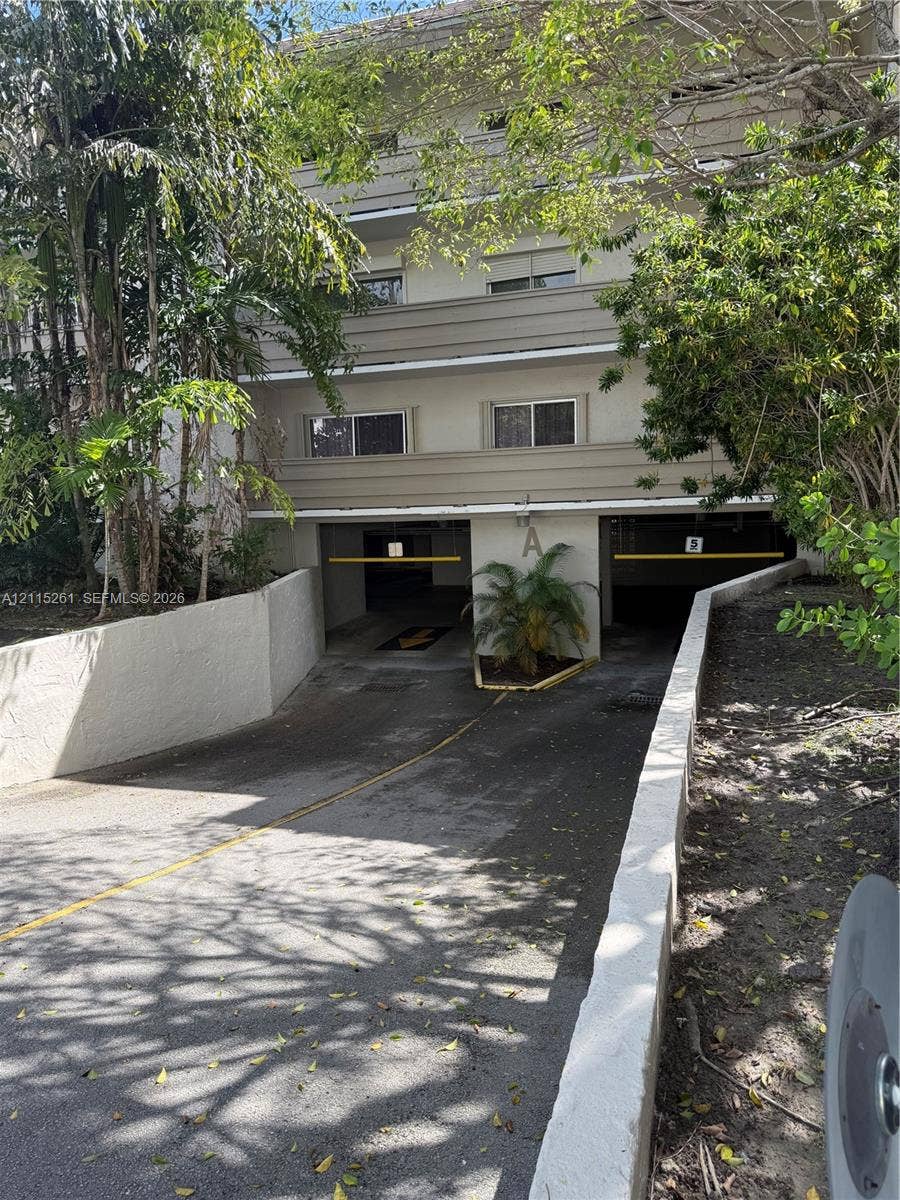 1205 Mariposa Avenue, #302, Coral Gables, Coral Gables, FL 33146 Multi-level residential exterior featuring a covered parking garage with two access bays, concrete retaining walls, and established tropical landscaping