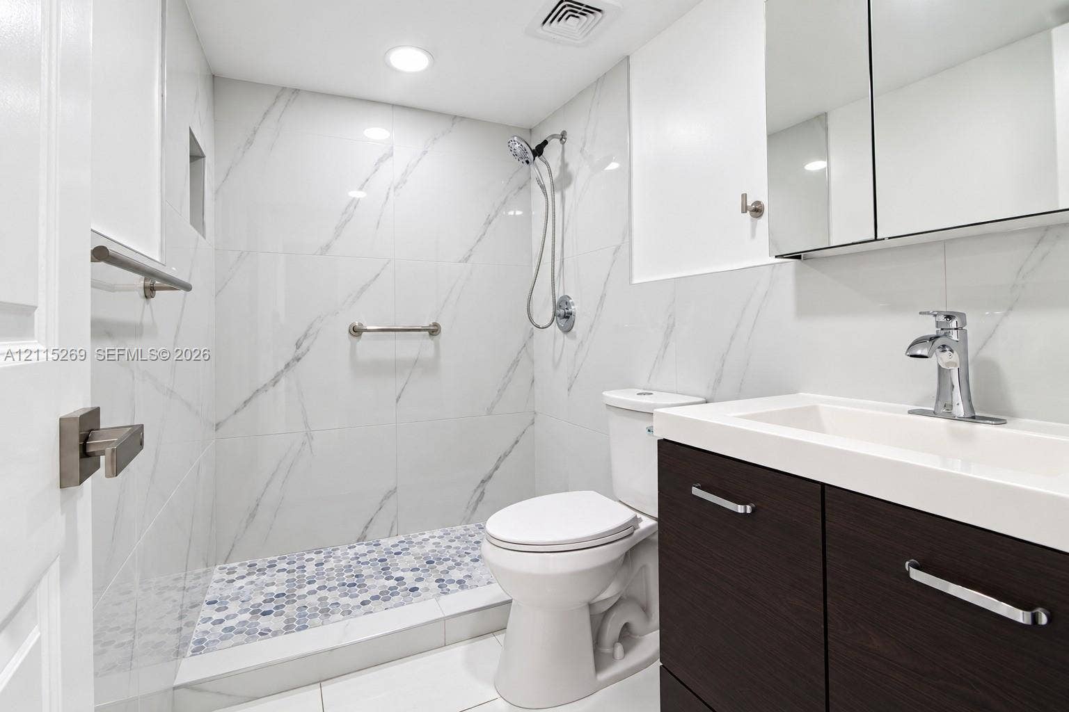 8615 NW 8th Street, #211, Miami, Miami, FL 33126 Bathroom featuring white wall tile with stone-pattern veining, a walk-in shower with penny-round floor tile, a dark wood-finish vanity with an integrated basin, and a mirrored medicine cabinet