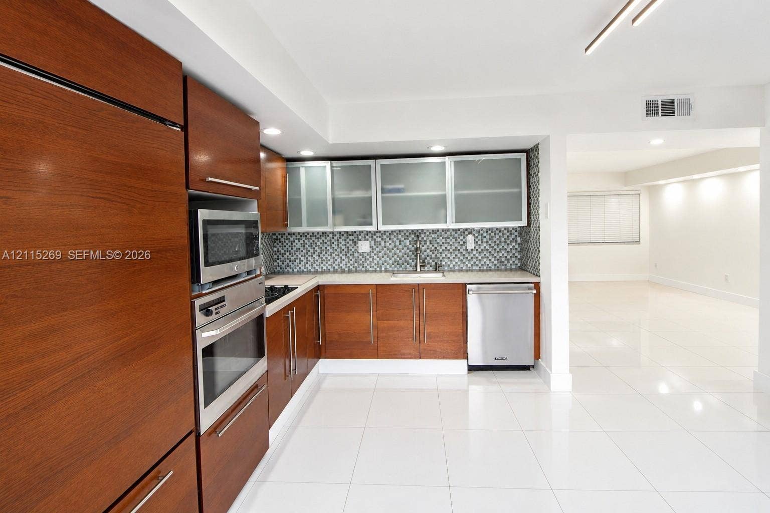 8615 NW 8th Street, #211, Miami, Miami, FL 33126 Kitchen featuring wood-finish cabinetry, stainless steel built-in oven and microwave, patterned tile backsplash, frosted-glass upper cabinet inserts, and polished tile flooring