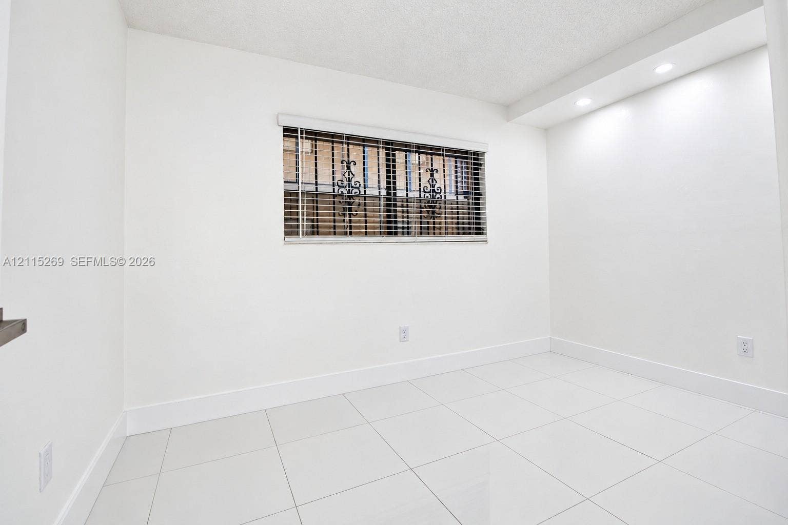 8615 NW 8th Street, #211, Miami, Miami, FL 33126 Bright room featuring white tile flooring, recessed ceiling lighting, and a window equipped with horizontal blinds and decorative metal security grilles