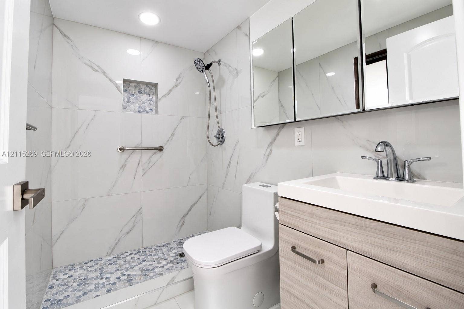 8615 NW 8th Street, #211, Miami, Miami, FL 33126 Walk-in shower with stone-finish tile surround, integrated shower niche, penny-tile floor, wood-finish vanity, and recessed medicine cabinet