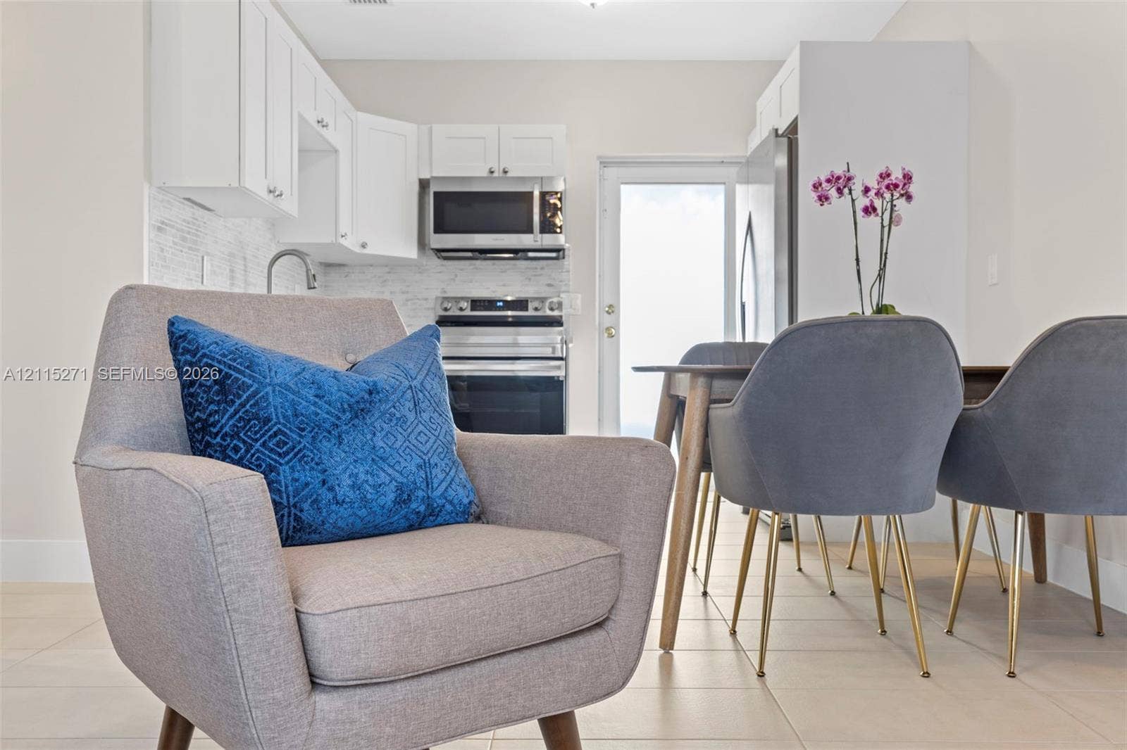 Kitchen featuring white shaker-style cabinetry, a stone-finish backsplash, stainless steel appliances, and tile flooring