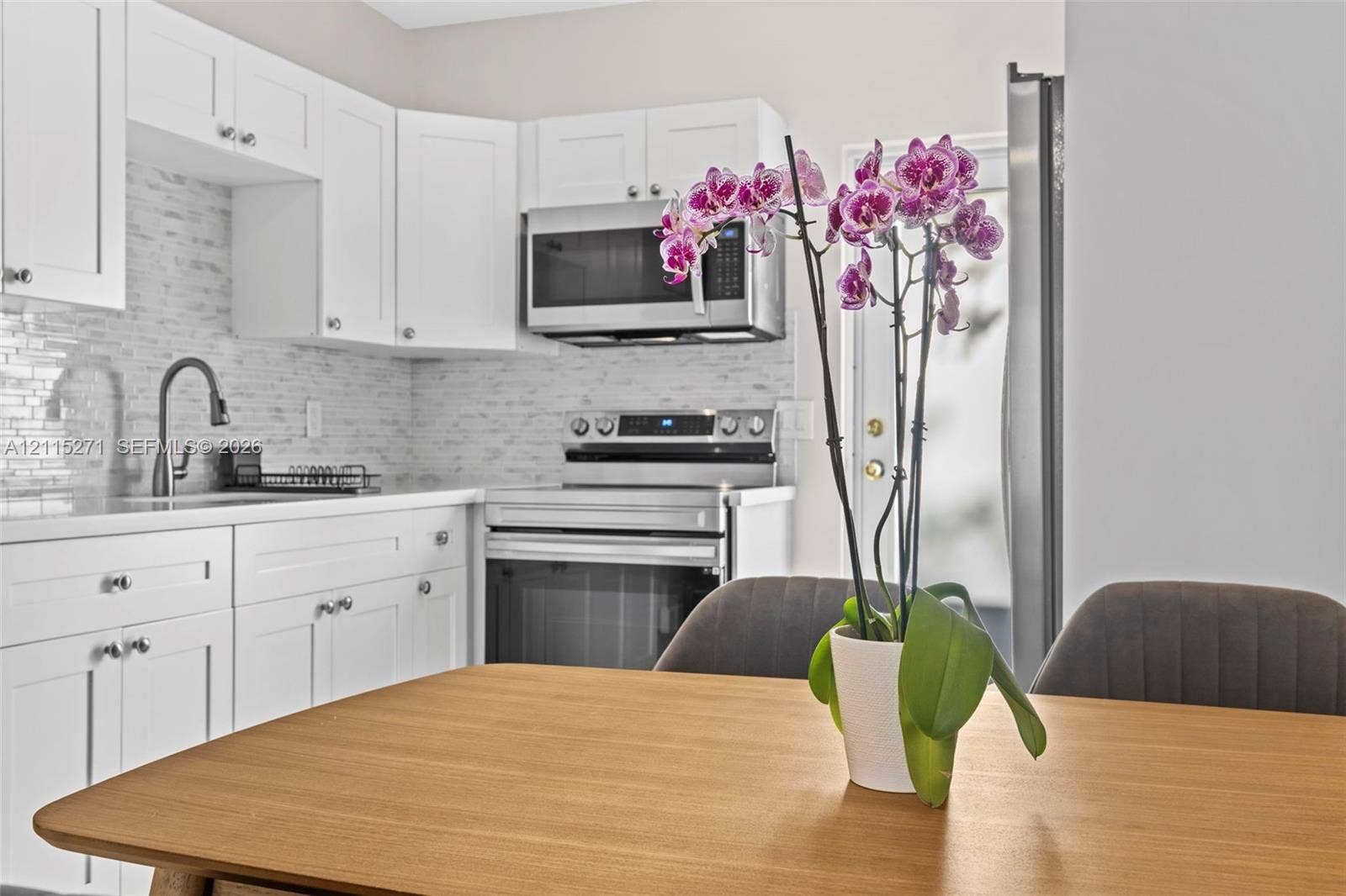Kitchen featuring white shaker-style cabinetry, a textured stone backsplash, stainless steel appliances, and a curved faucet
