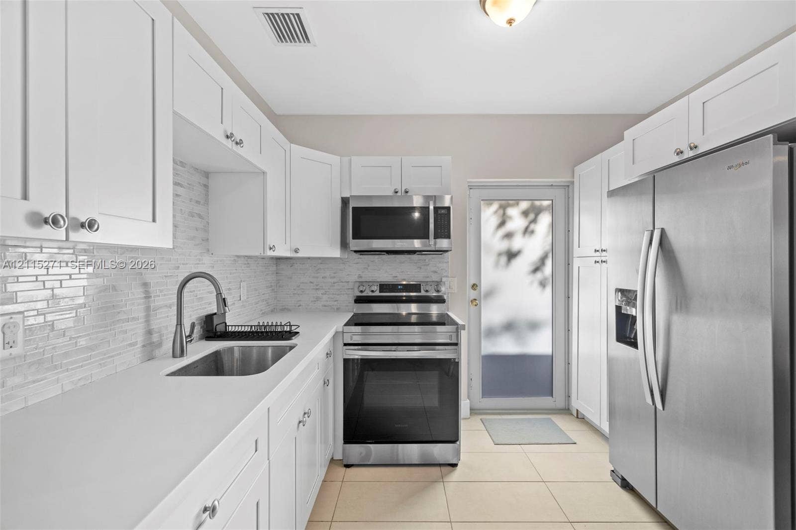 Kitchen featuring white shaker-style cabinetry, solid-surface countertops, textured tile backsplash, stainless steel appliances, and ceramic tile flooring