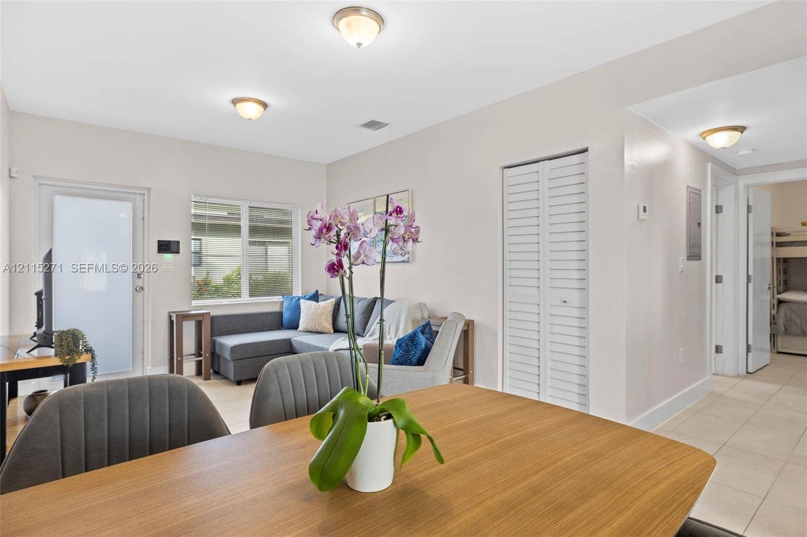 Open-concept interior featuring light-toned tile flooring, recessed dome-style ceiling lighting, louvered closet doors, and large dual-pane windows