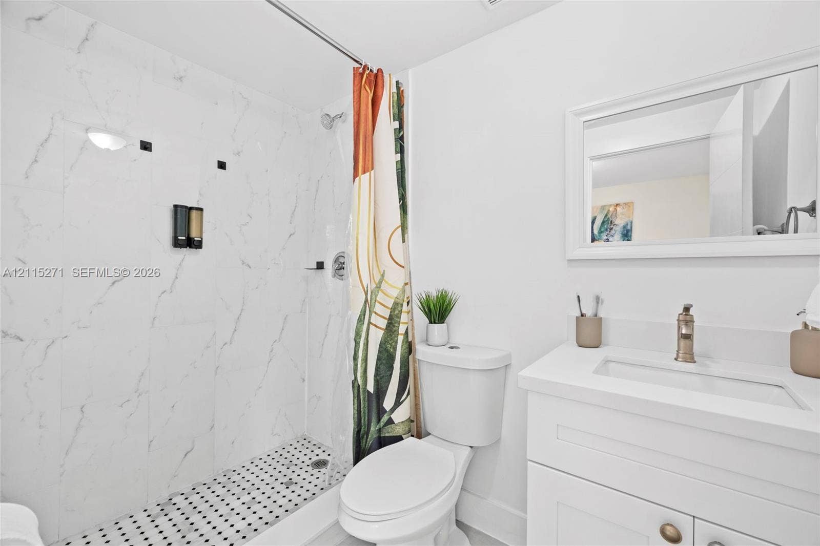 Bathroom featuring a walk-in shower with stone-patterned tile surround, penny-tile flooring, a vanity with a white countertop and integrated sink, and a framed wall mirror