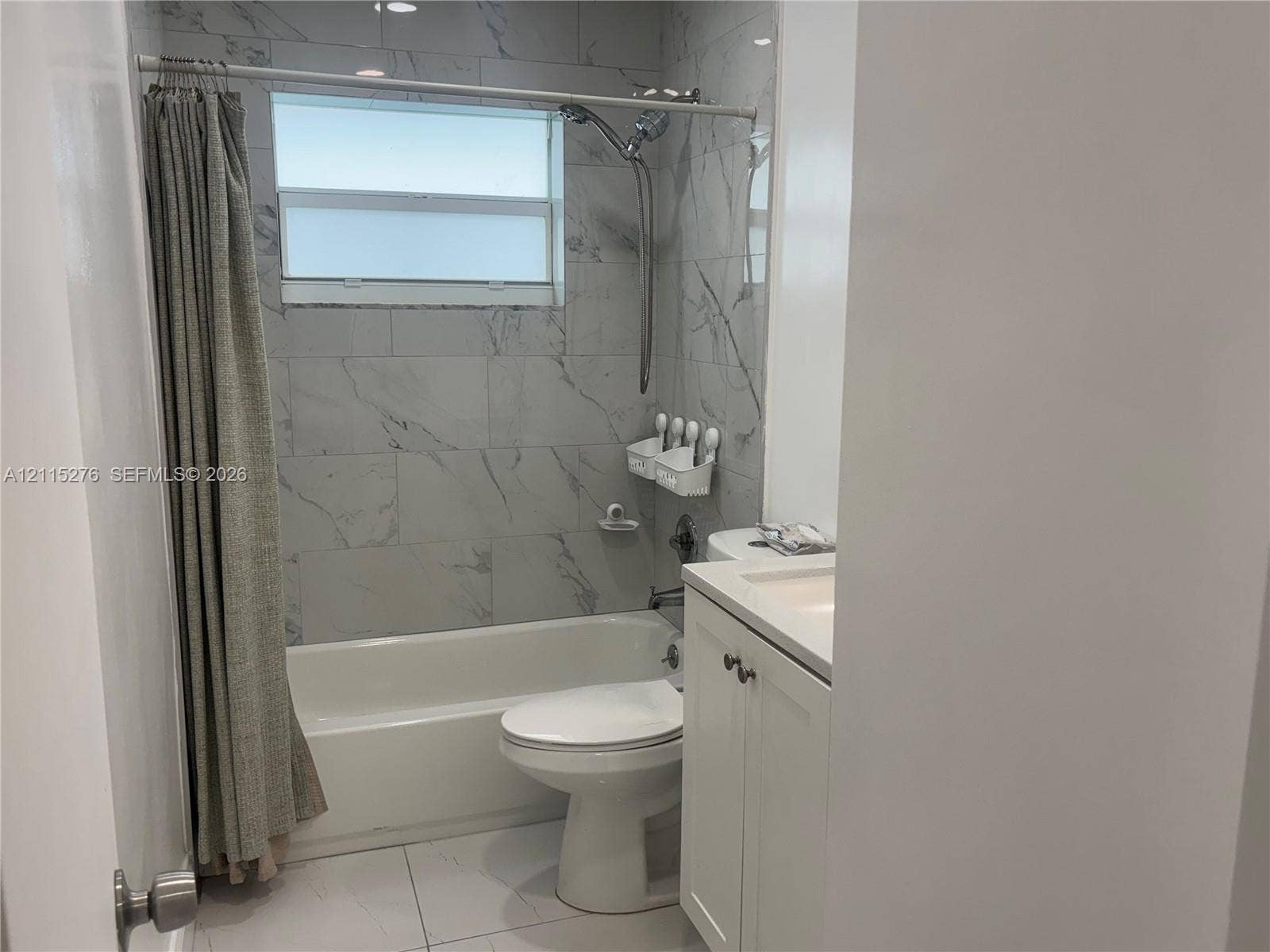 Davie, FL 33314 Bathroom featuring full-height stone-finish wall tile, a built-in bathtub, a shaker-style vanity with an integrated basin, and a window