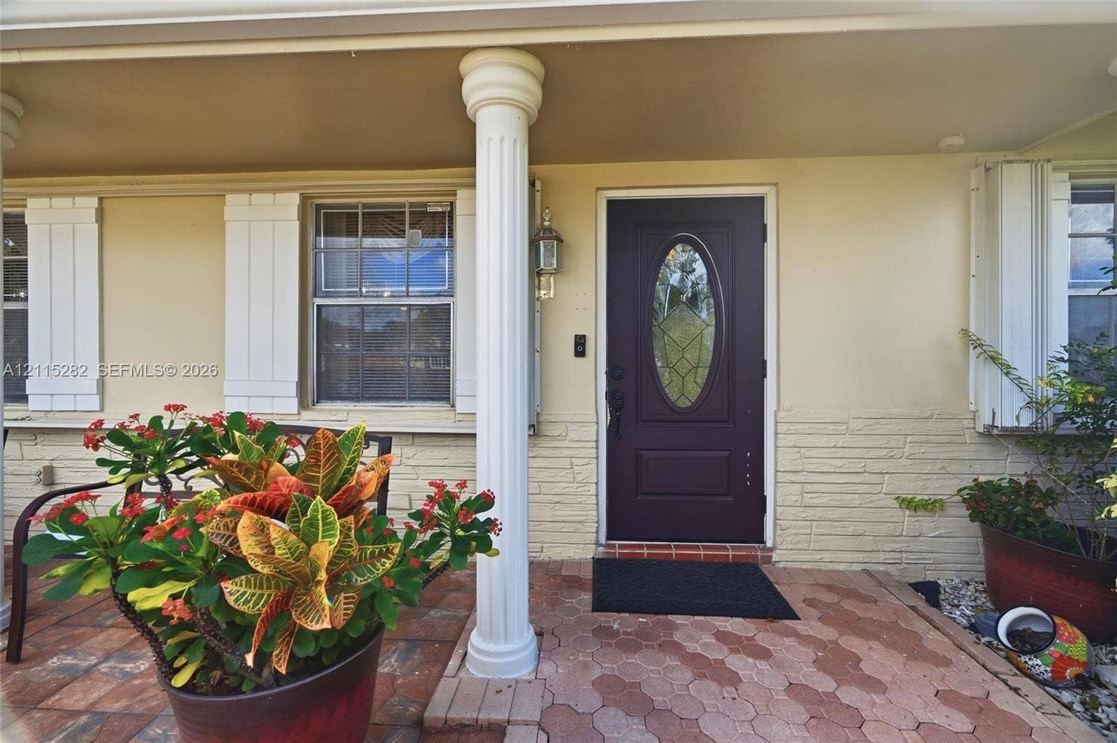 Covered entryway featuring a fluted column, stone-finish exterior wall, paver flooring, and a central entry door with a decorative glass insert