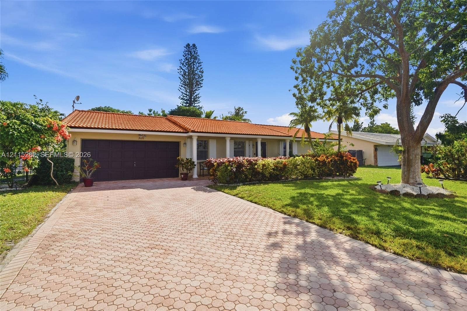 Single-story exterior featuring a clay tile roof, paver driveway, covered entryway with columns, and mature landscaping