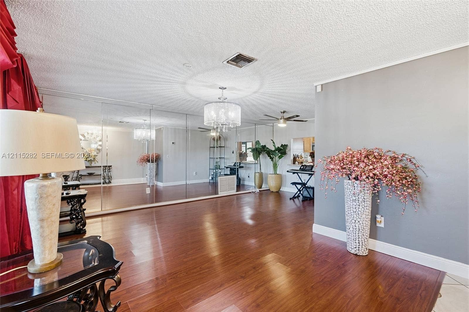 Open floor plan featuring wood-finish flooring, floor-to-ceiling mirror wall, and a multi-light drum chandelier
