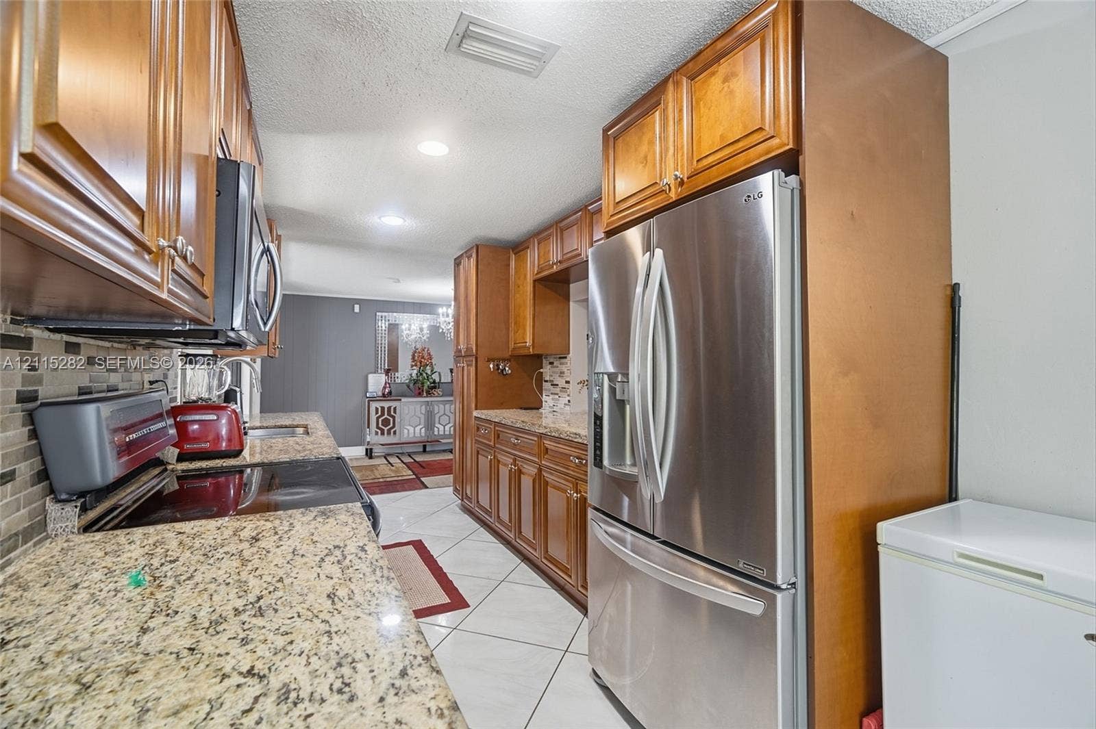 Kitchen featuring wood cabinetry, stone countertops, stainless steel refrigerator, mosaic tile backsplash, and tile flooring